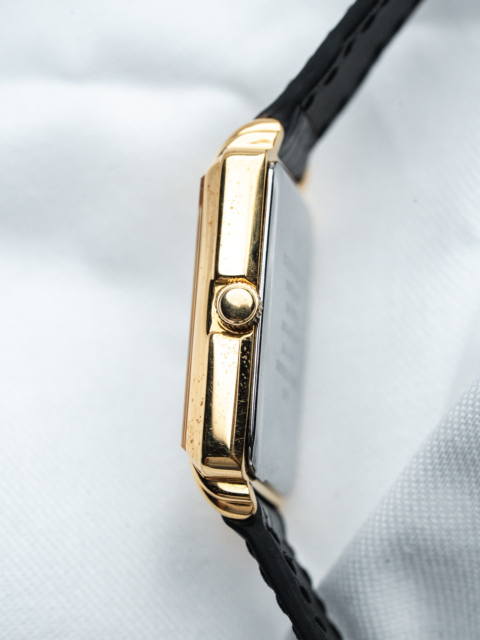 Vintage Cartier Tank watch with gold case and black leather strap, side view on white background
