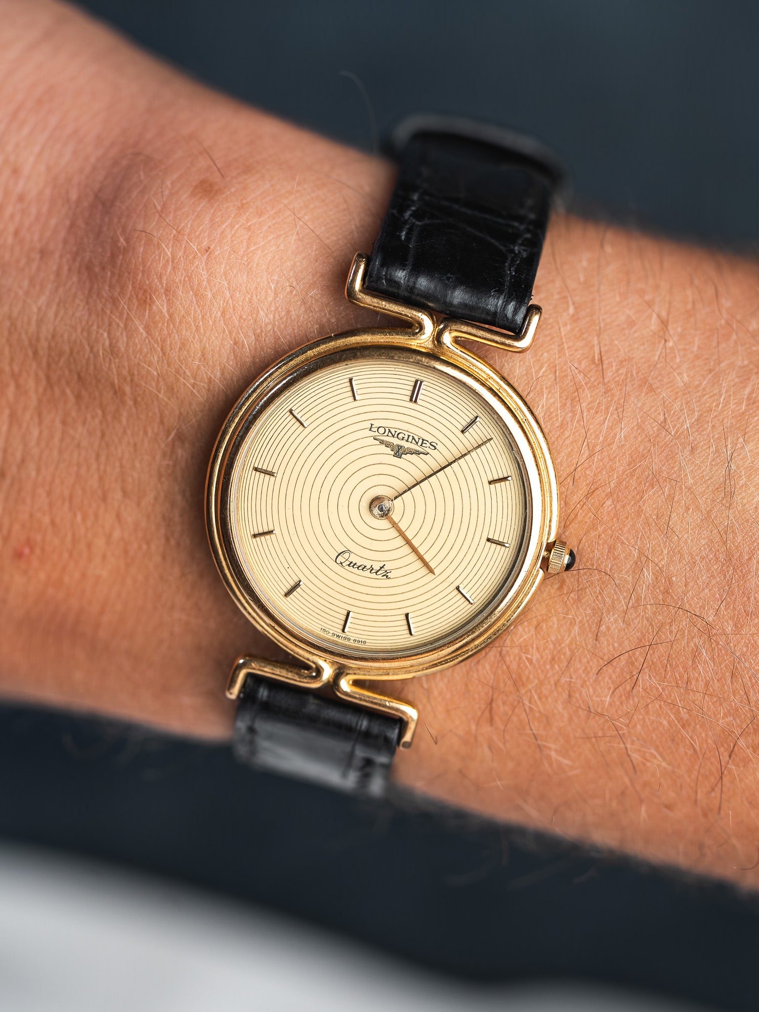 Longines vintage quartz watch with gold case, sunburst dial, and black leather strap on wrist