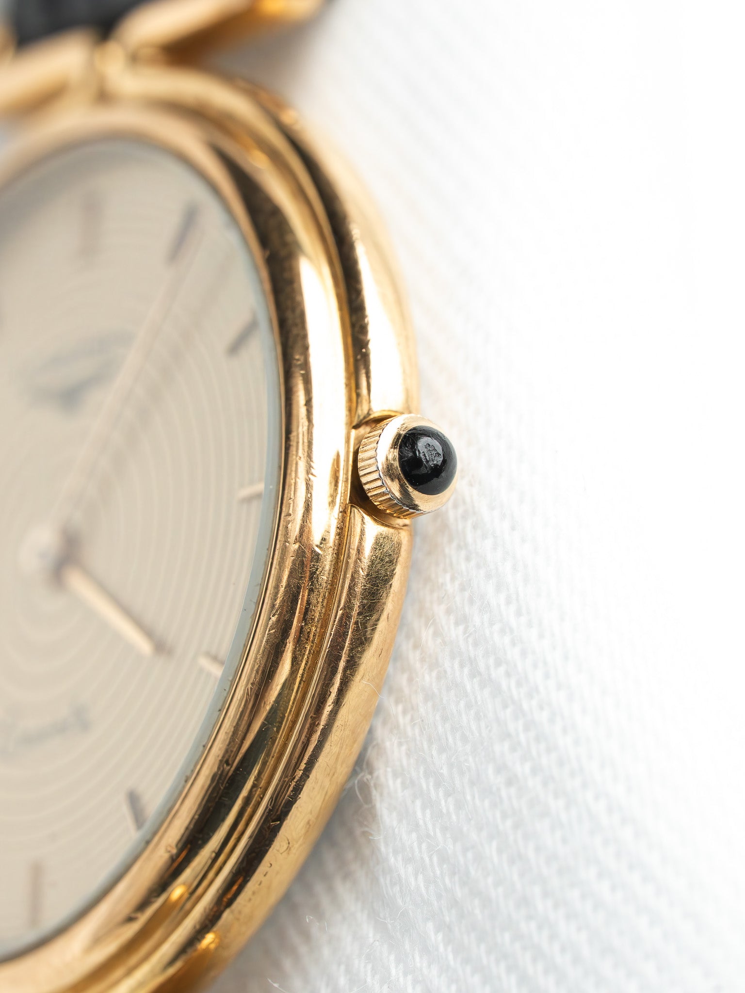 Vintage gold watch with white dial and black crown, close-up on textured surface