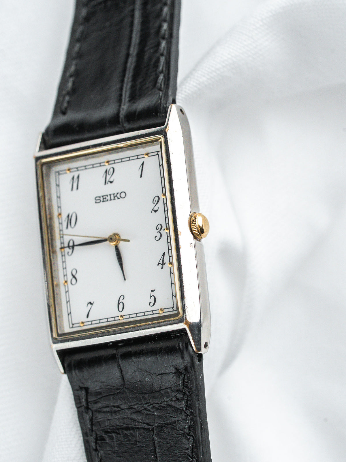 Seiko montre vintage avec boîtier rectangulaire, cadran blanc, bracelet en cuir noir sur fond blanc