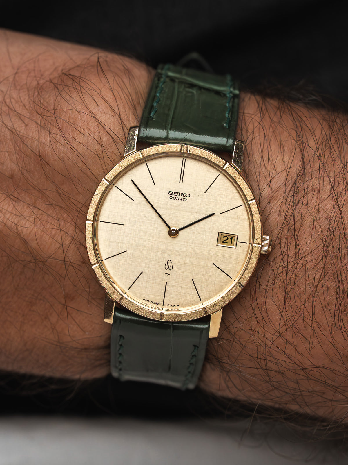 Montre Seiko Quartz vintage au cadran doré et bracelet en cuir vert foncé.