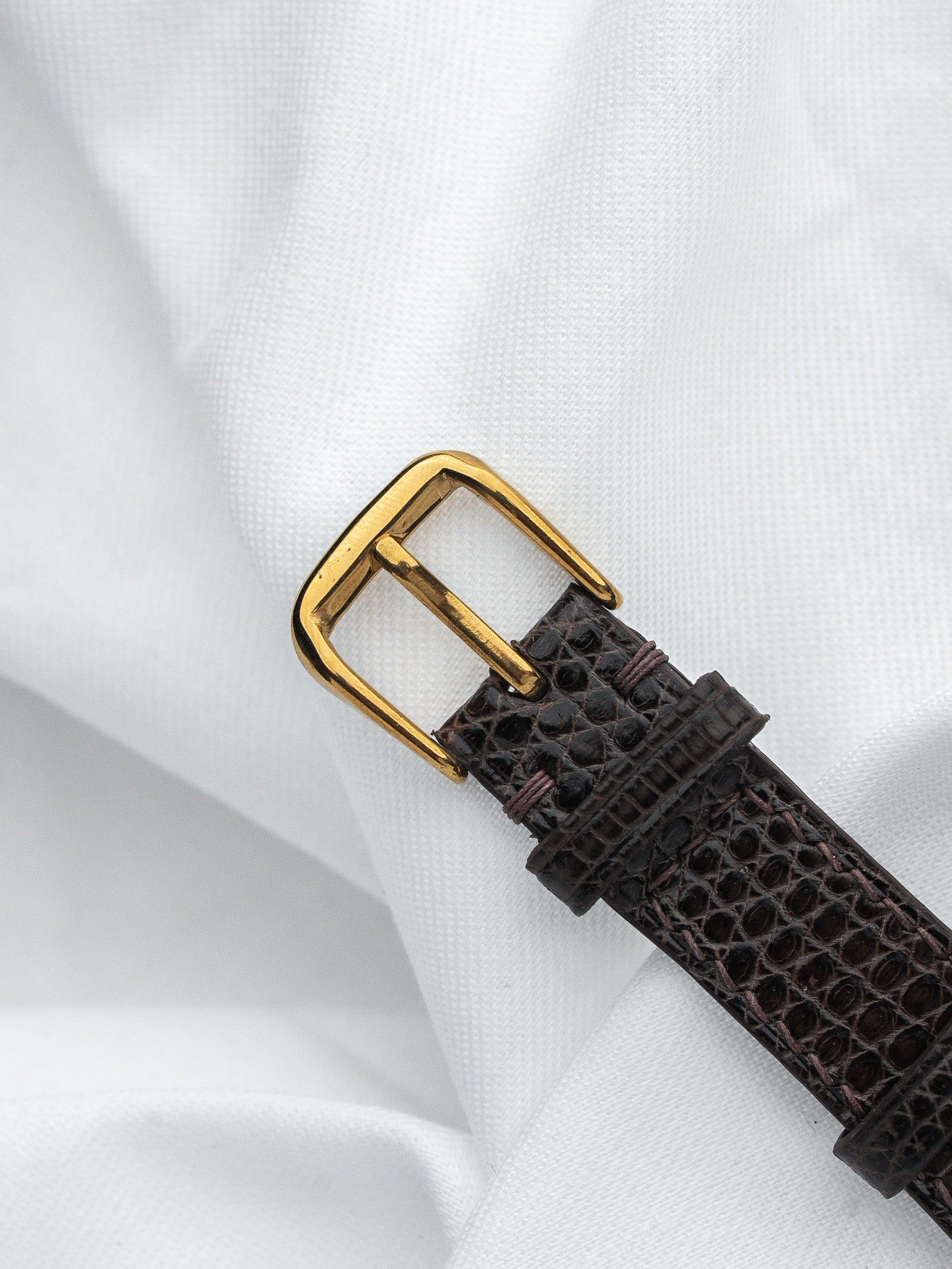 Vintage watch strap with brown alligator texture and gold buckle on white fabric