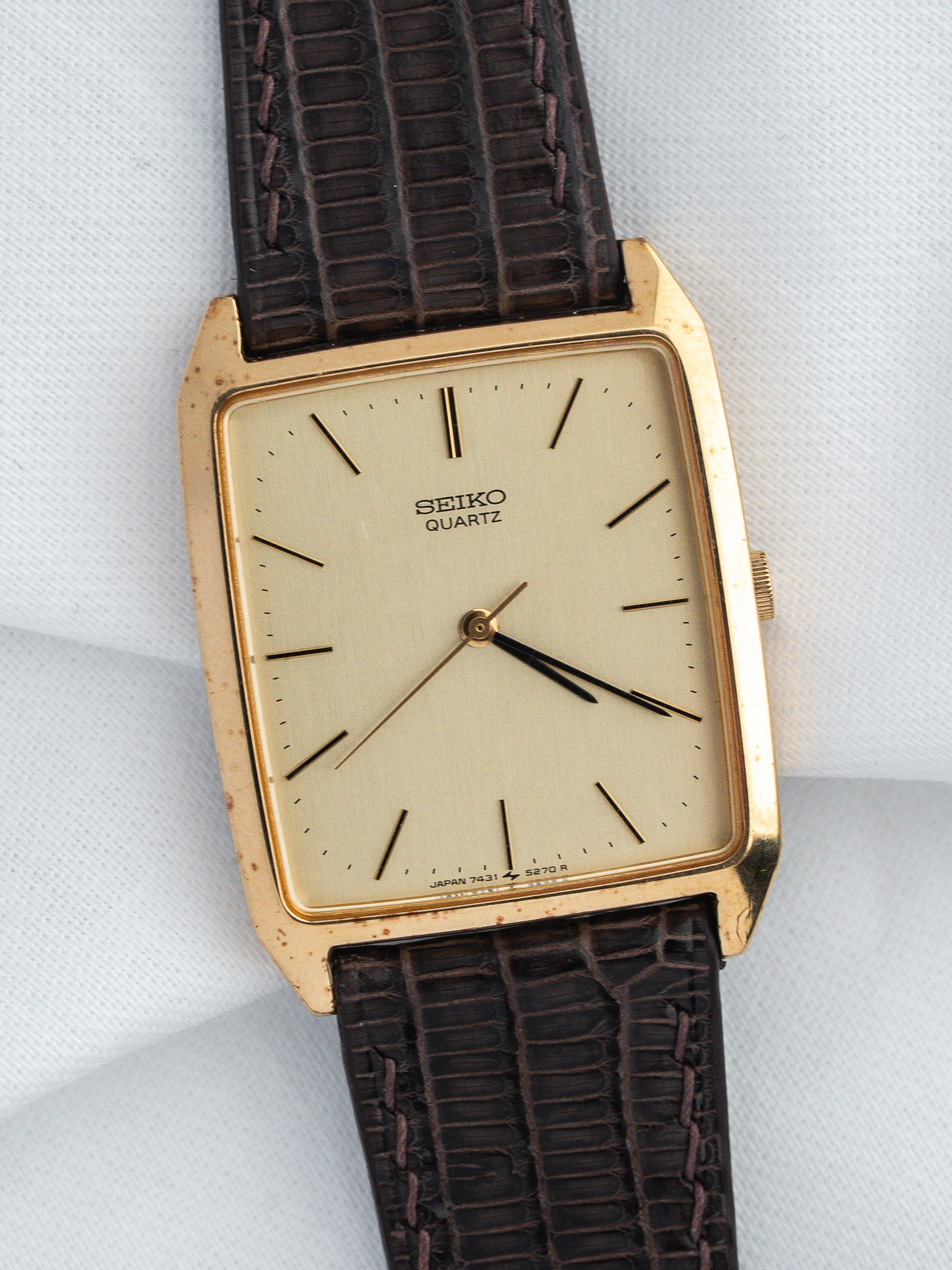 Vintage Seiko Quartz watch with gold case, cream dial, and brown textured strap on white background