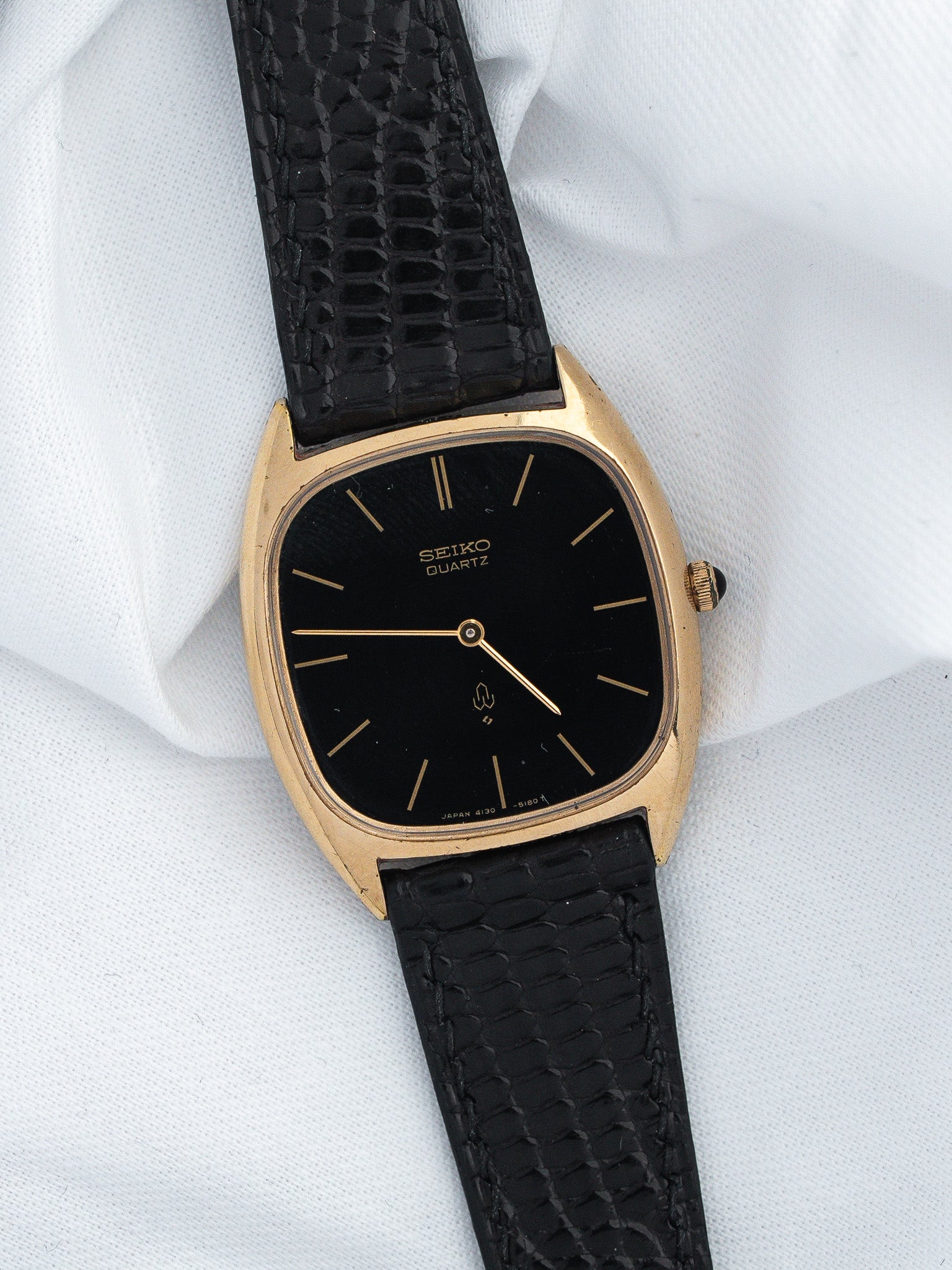 Seiko Quartz vintage watch with gold case, black dial, and textured black strap on white fabric