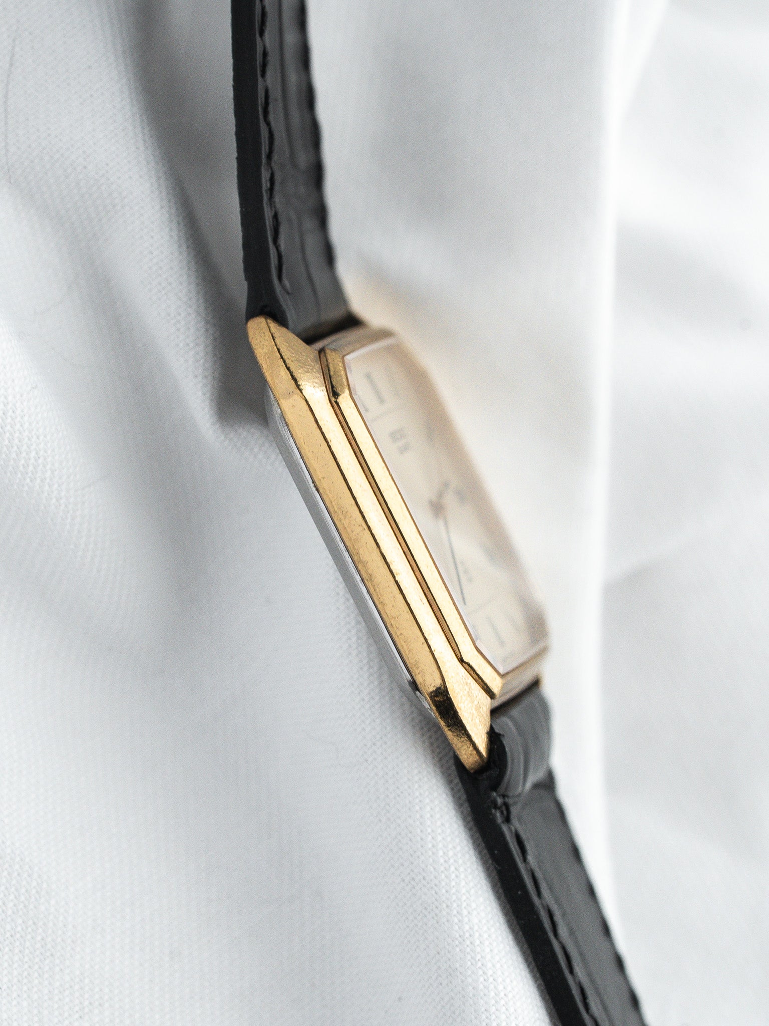Vintage Cartier Tank watch with gold case, black leather strap, white dial on white fabric