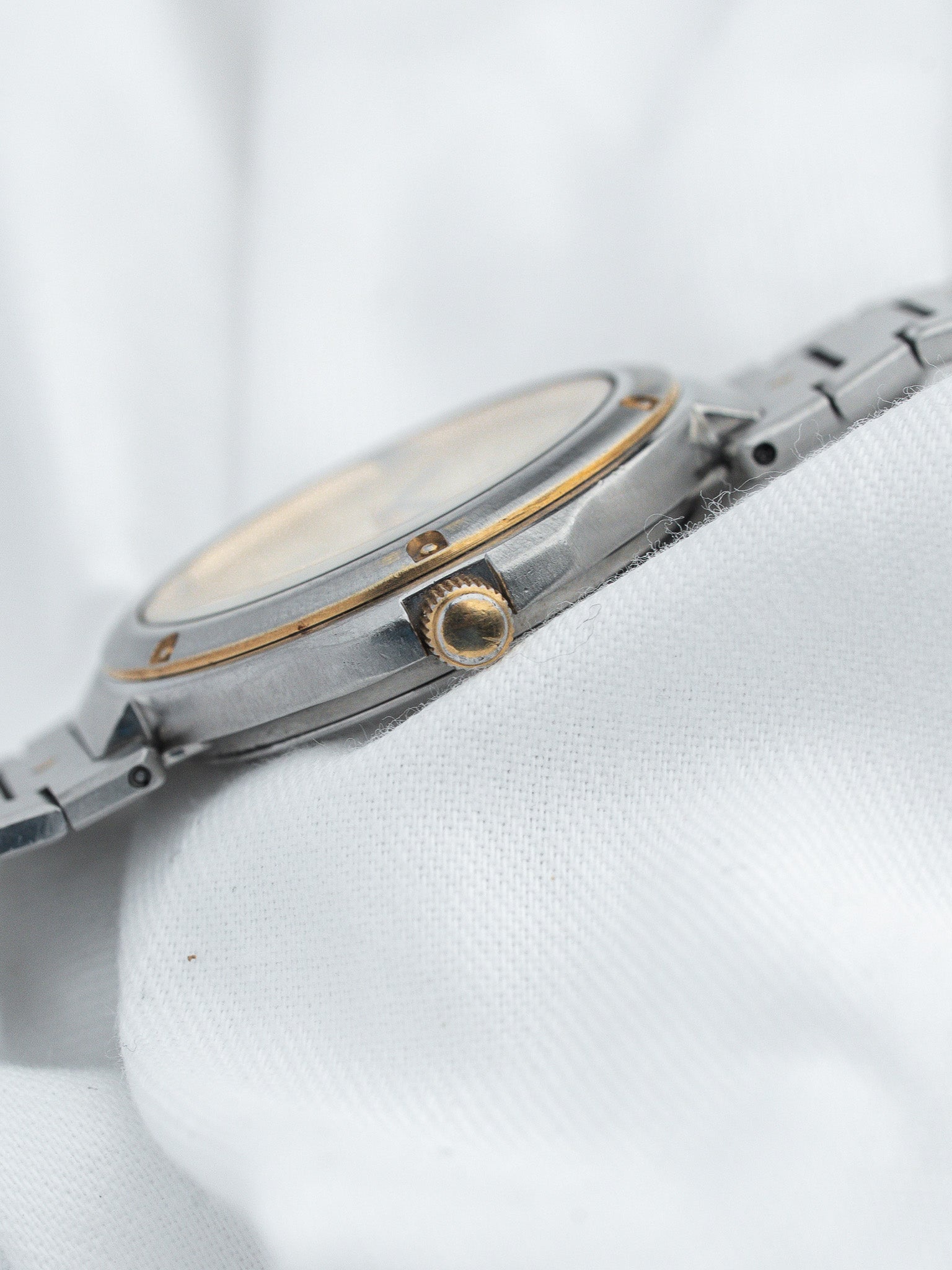 Vintage Omega watch with steel and gold case, white dial, on white fabric
