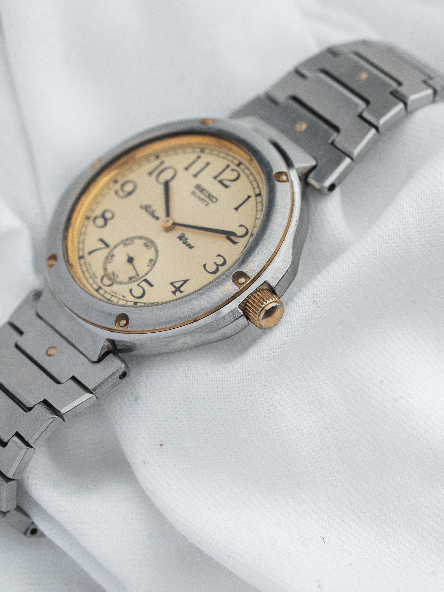 Seiko vintage watch with cream dial, gold accents, and steel bracelet on white fabric