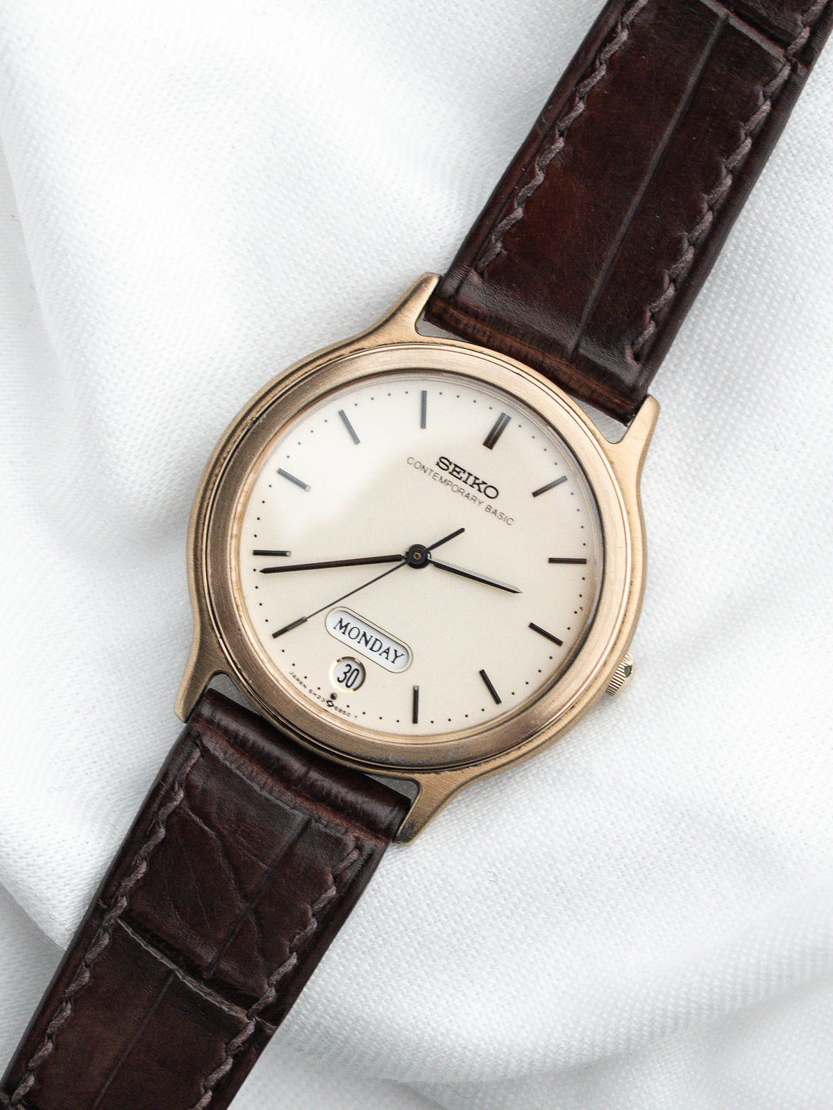 Montre Seiko vintage avec cadran blanc, boîtier doré et bracelet en cuir marron.