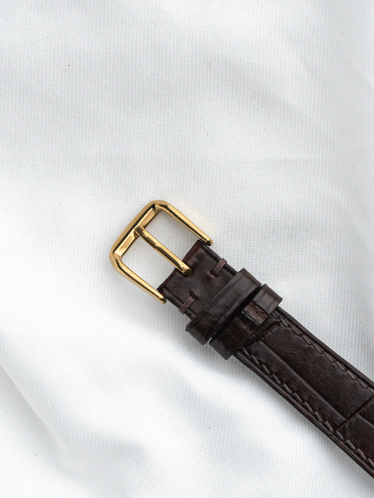 Bracelet de montre en cuir marron avec boucle dorée sur fond blanc