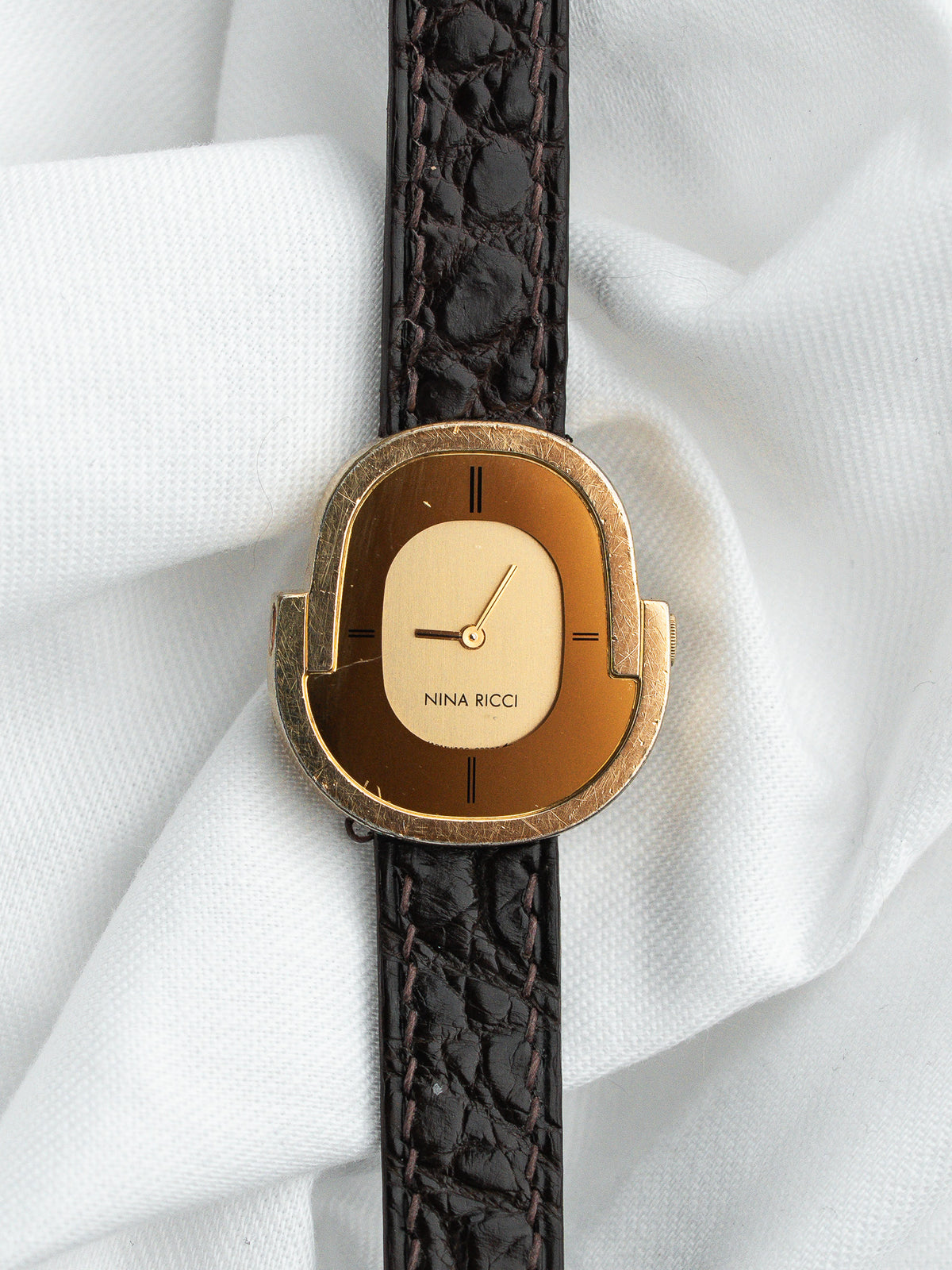 Montre Nina Ricci vintage avec boîtier doré et bracelet en cuir brun texturé.