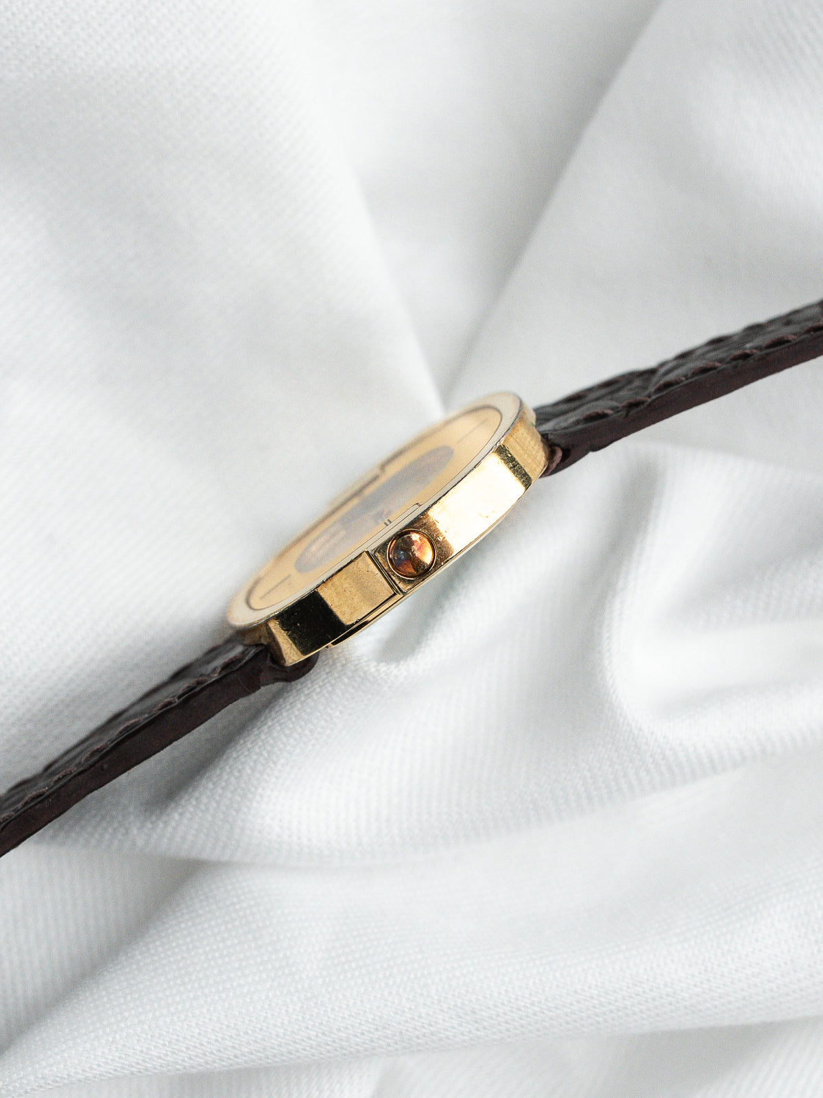 Vue de profil d'une montre vintage dorée avec un bracelet en cuir marron.