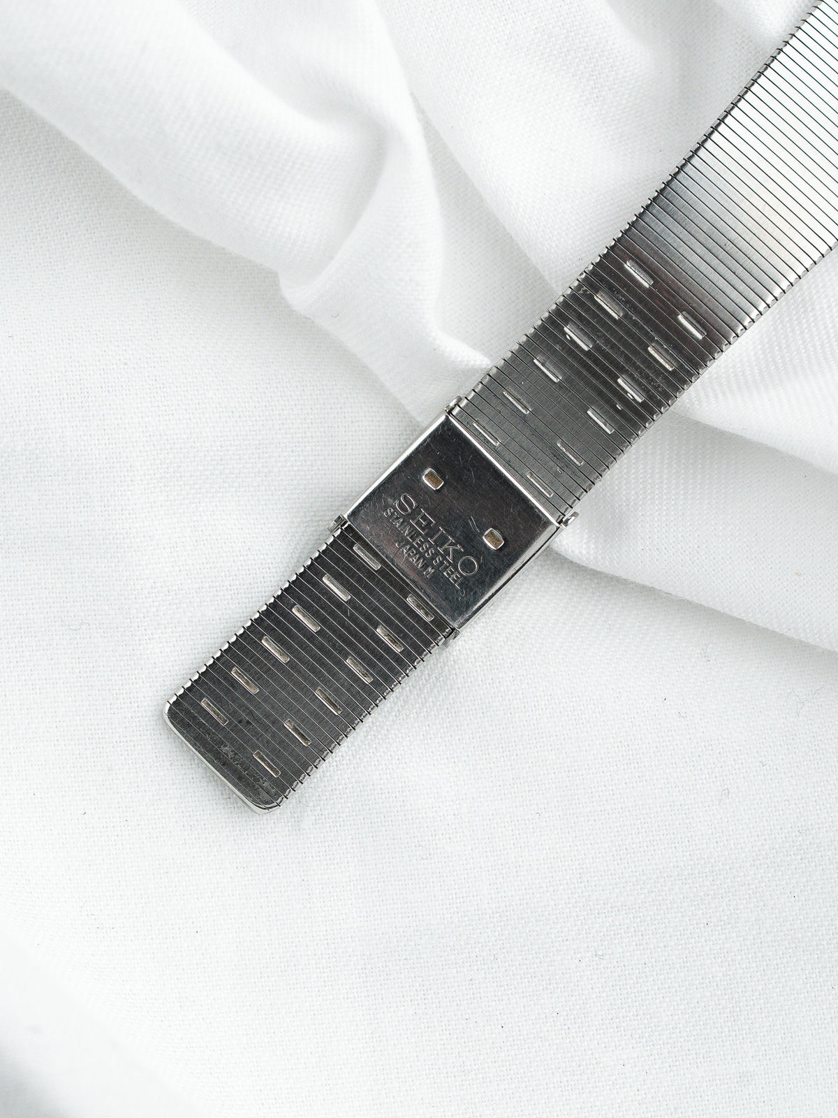 Bracelet en acier inoxydable Seiko avec fermoir déployant sur un fond de tissu blanc.