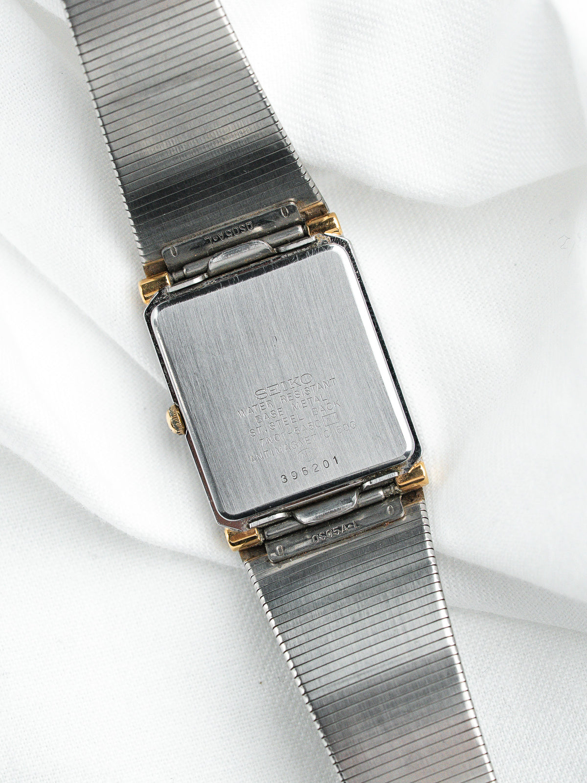 Dos d'une montre Seiko vintage avec bracelet métallique argenté sur fond blanc.