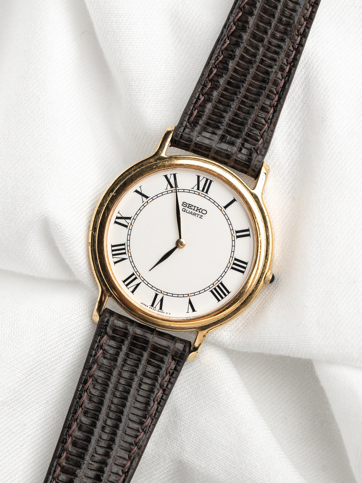 Montre Seiko Quartz vintage avec boîtier doré, cadran blanc et bracelet en cuir marron.