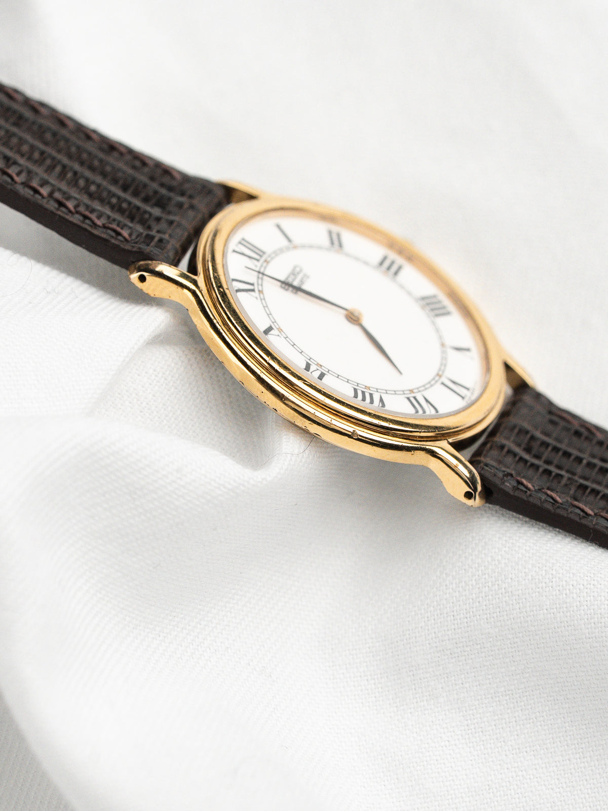 Montre vintage avec boîtier doré, cadran blanc à chiffres romains et bracelet en cuir brun.