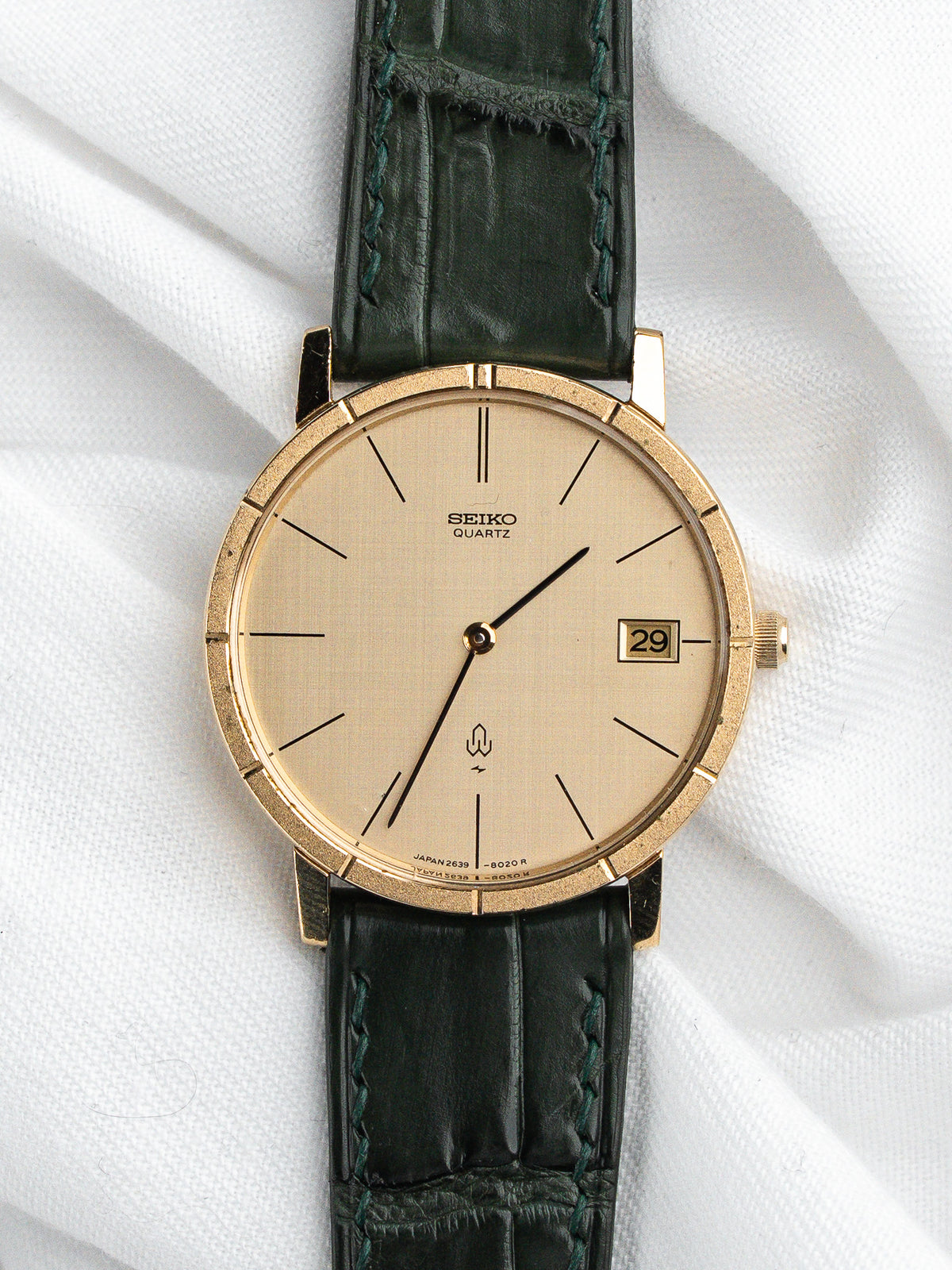 Montre Seiko Quartz vintage au cadran doré et bracelet en cuir vert foncé.
