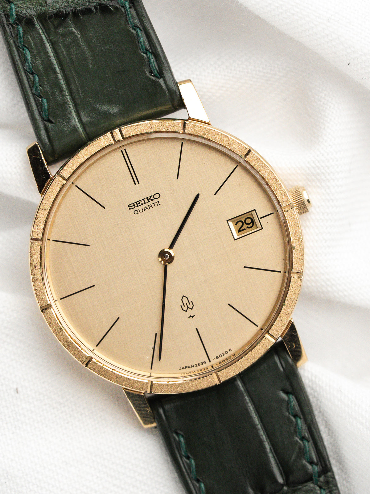 Montre Seiko Quartz vintage au boîtier doré avec un bracelet en cuir vert.
