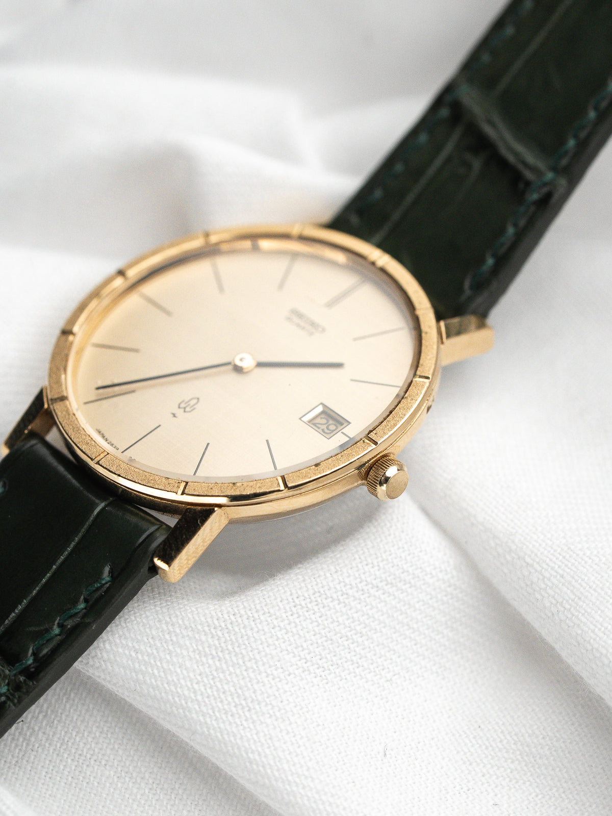 Montre vintage au boîtier doré, cadran champagne et bracelet en cuir vert foncé.