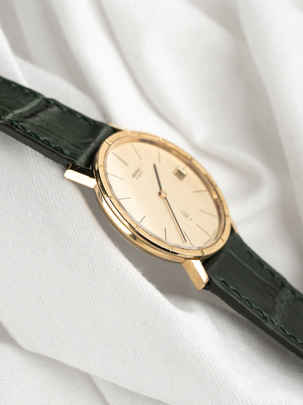 Montre vintage au boîtier doré, cadran blanc et bracelet en cuir vert foncé.