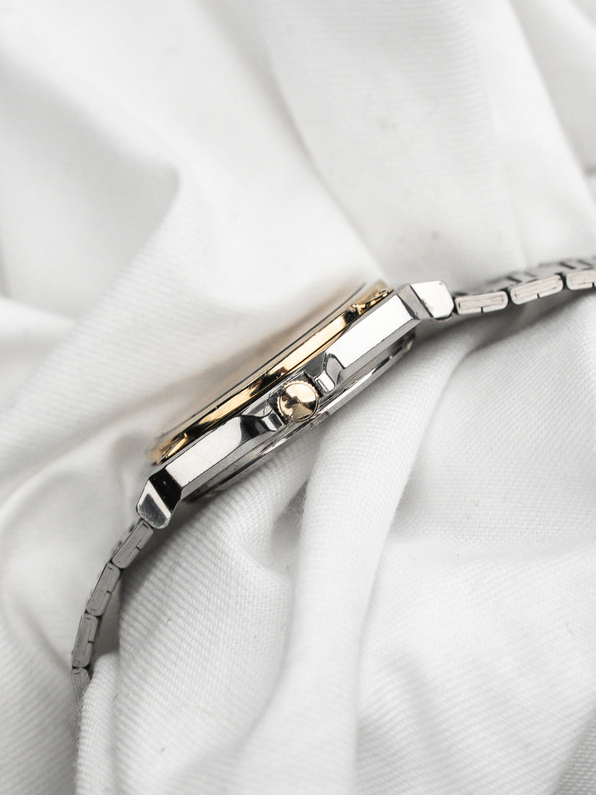 Profile view of a vintage watch in steel and gold on a white fabric background