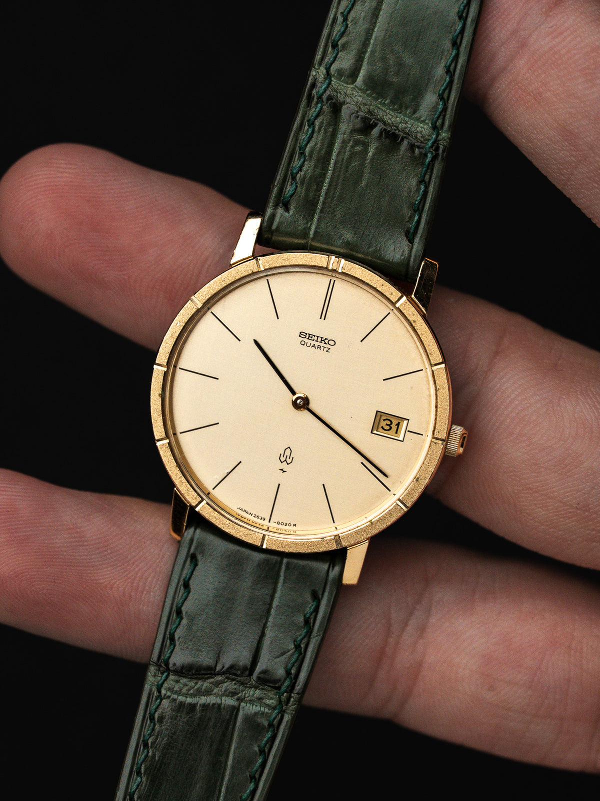 Montre Seiko Quartz vintage au cadran champagne et bracelet en cuir vert foncé.
