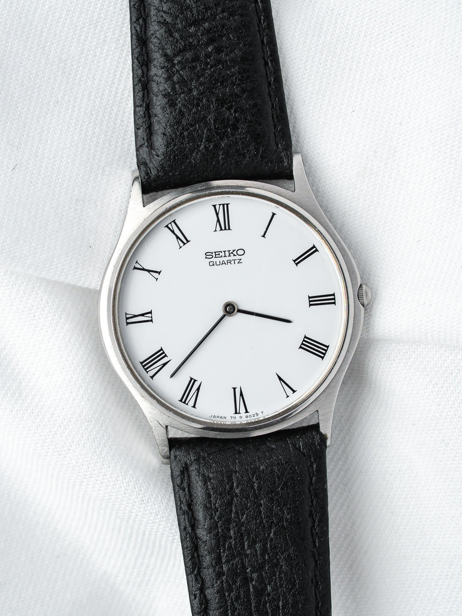 Seiko Quartz vintage watch with white dial, Roman numerals, black leather strap on white background