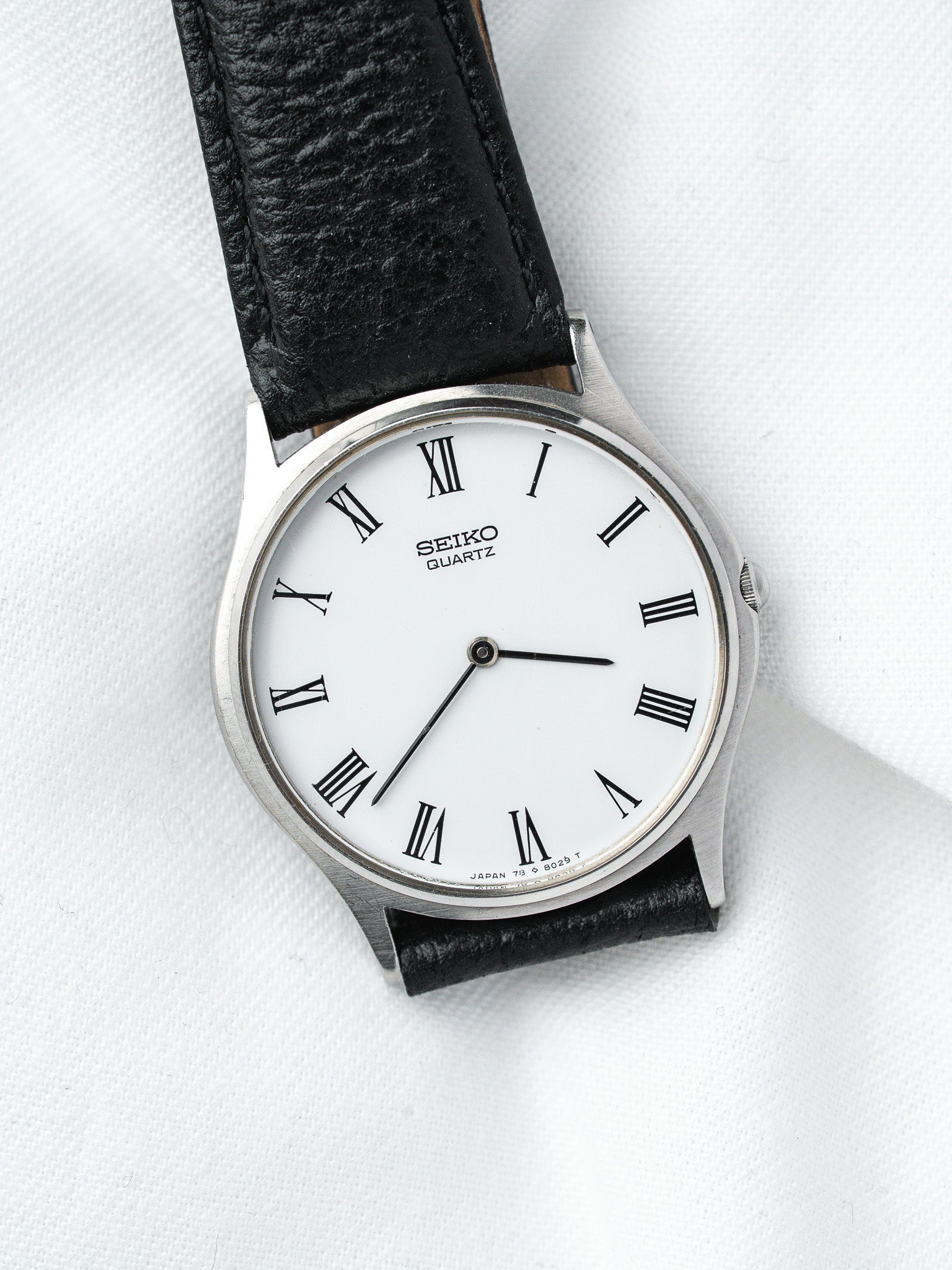 Seiko Quartz vintage watch with white dial, Roman numerals, black leather strap on white background