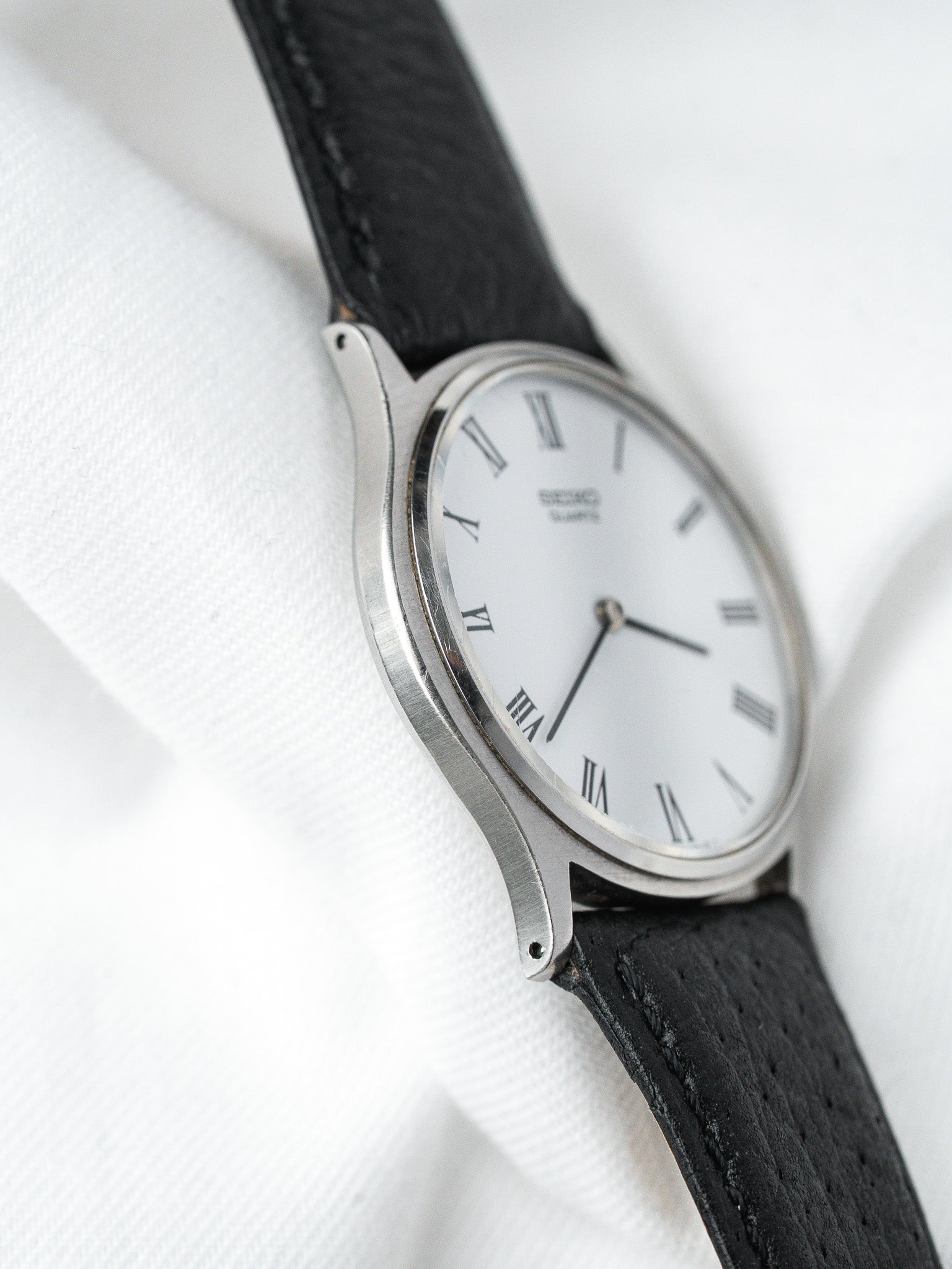 Seiko vintage watch with white dial, Roman numerals, black leather strap on white fabric