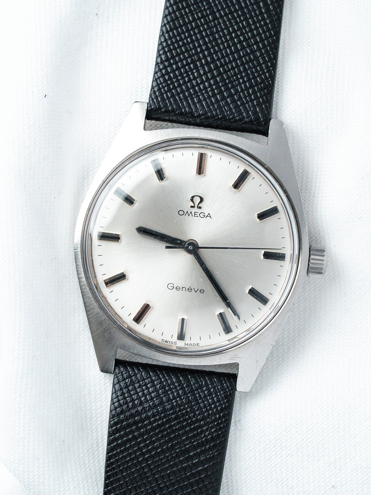 Omega Genève vintage watch with silver dial, black indices, and textured black strap