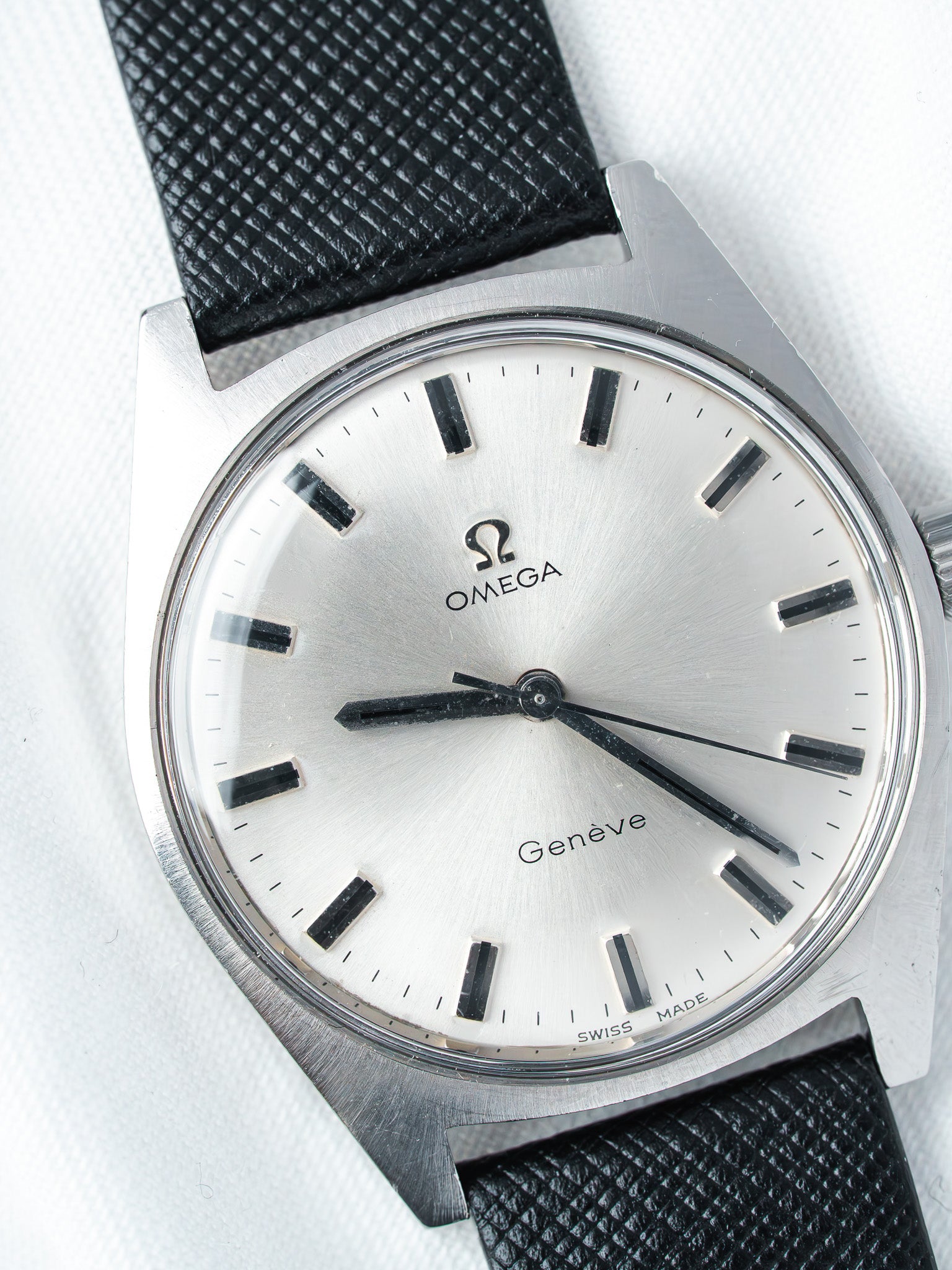 Omega Genève vintage watch with silver dial, black markers, and textured black strap