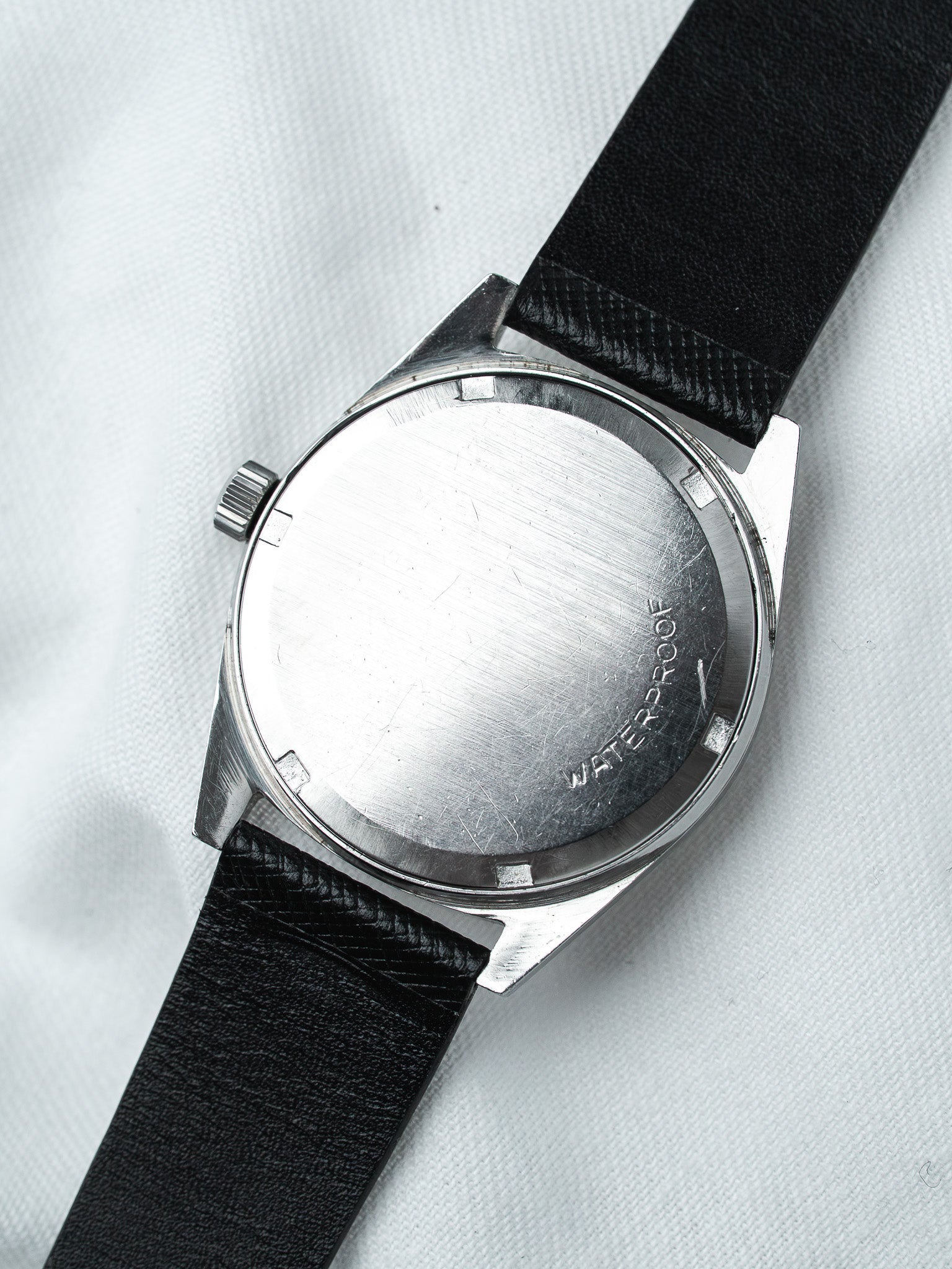 Vintage watch with stainless steel case, black leather strap, and waterproof engraving on case back