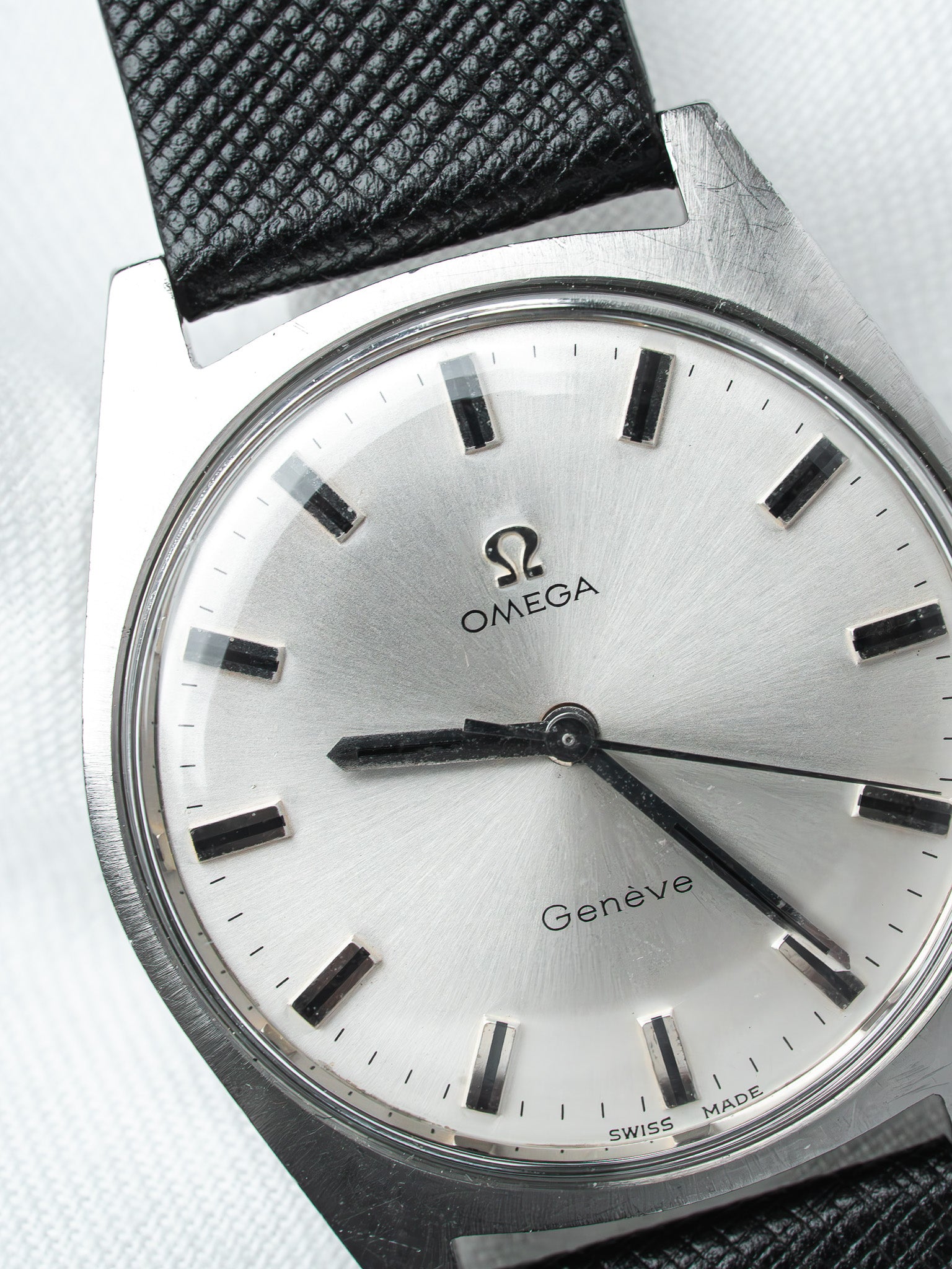 Omega Genève vintage watch with silver dial, black markers, and textured black strap