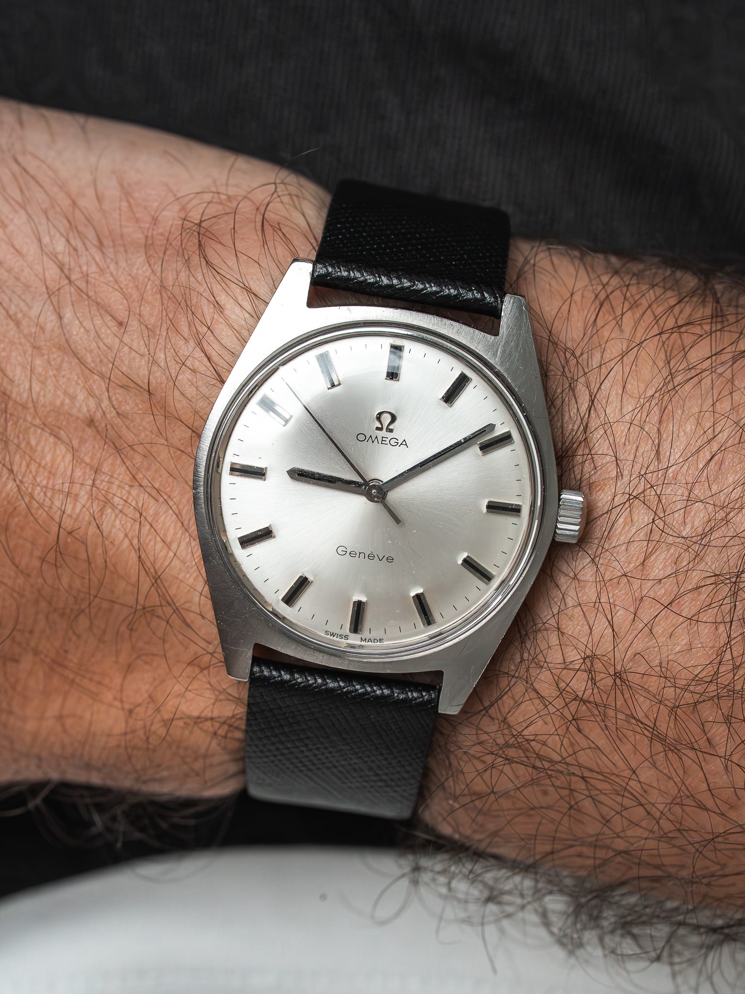 Omega Genève vintage watch with silver dial and black leather strap on wrist