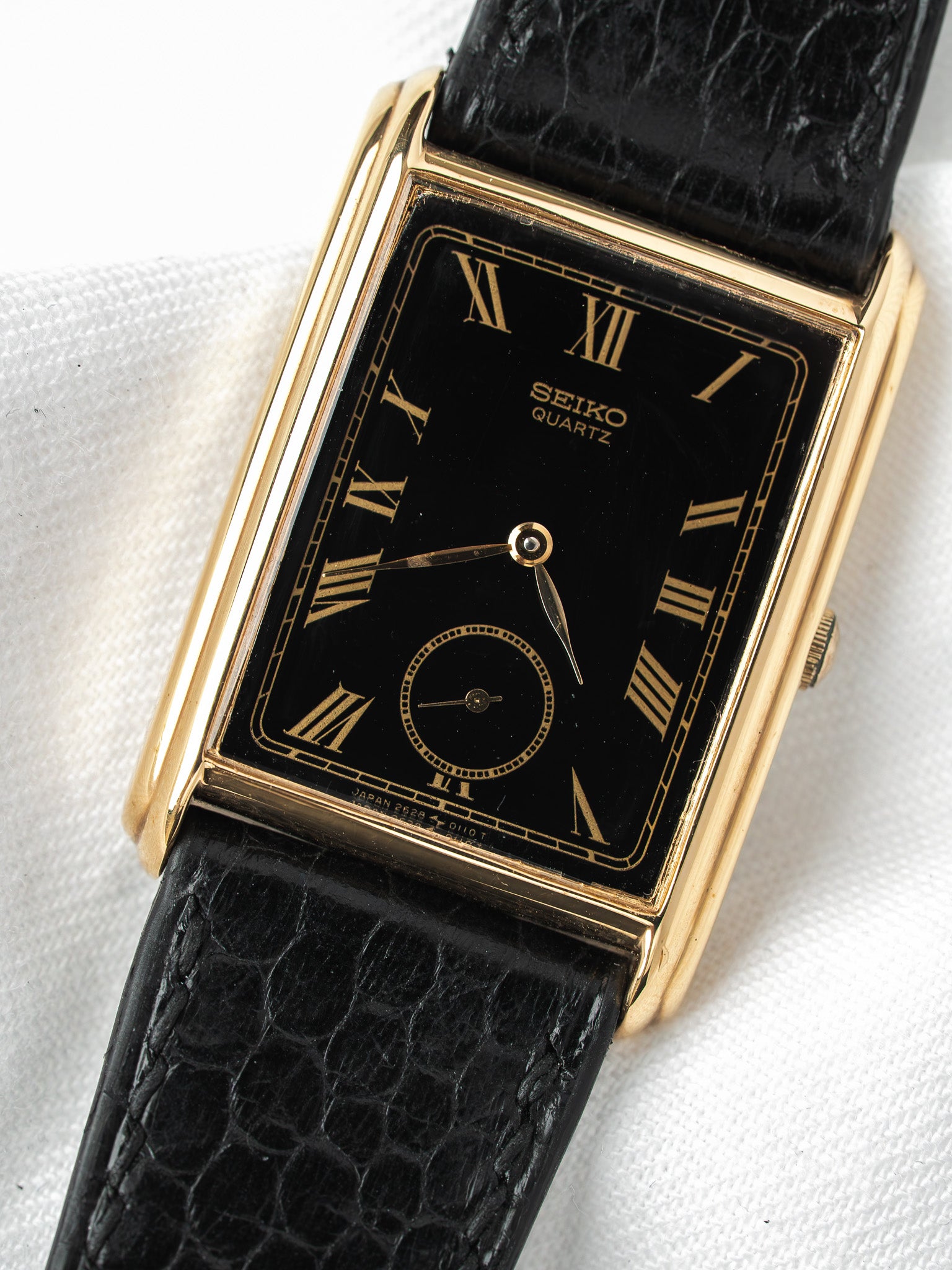 Seiko Quartz vintage watch with gold case, black dial, Roman numerals, and black leather strap