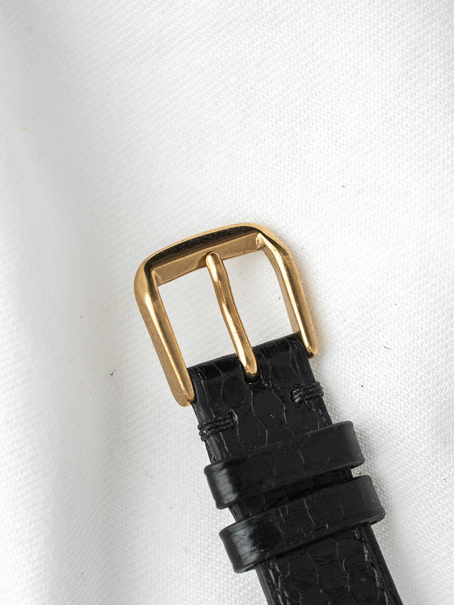 Black alligator leather watch strap with gold buckle on white background