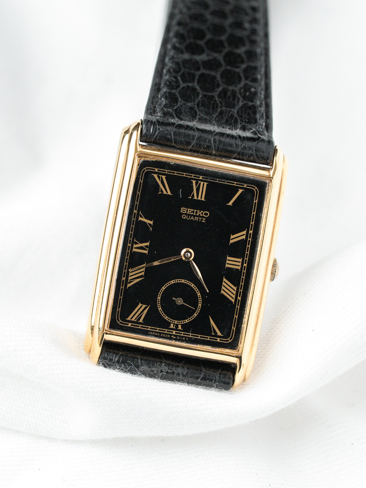 Seiko Quartz vintage watch with gold case, black dial, Roman numerals, and textured strap