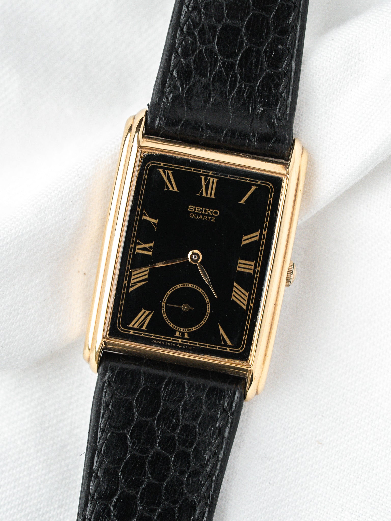 Seiko Quartz vintage watch with gold case, black dial, Roman numerals, and textured strap