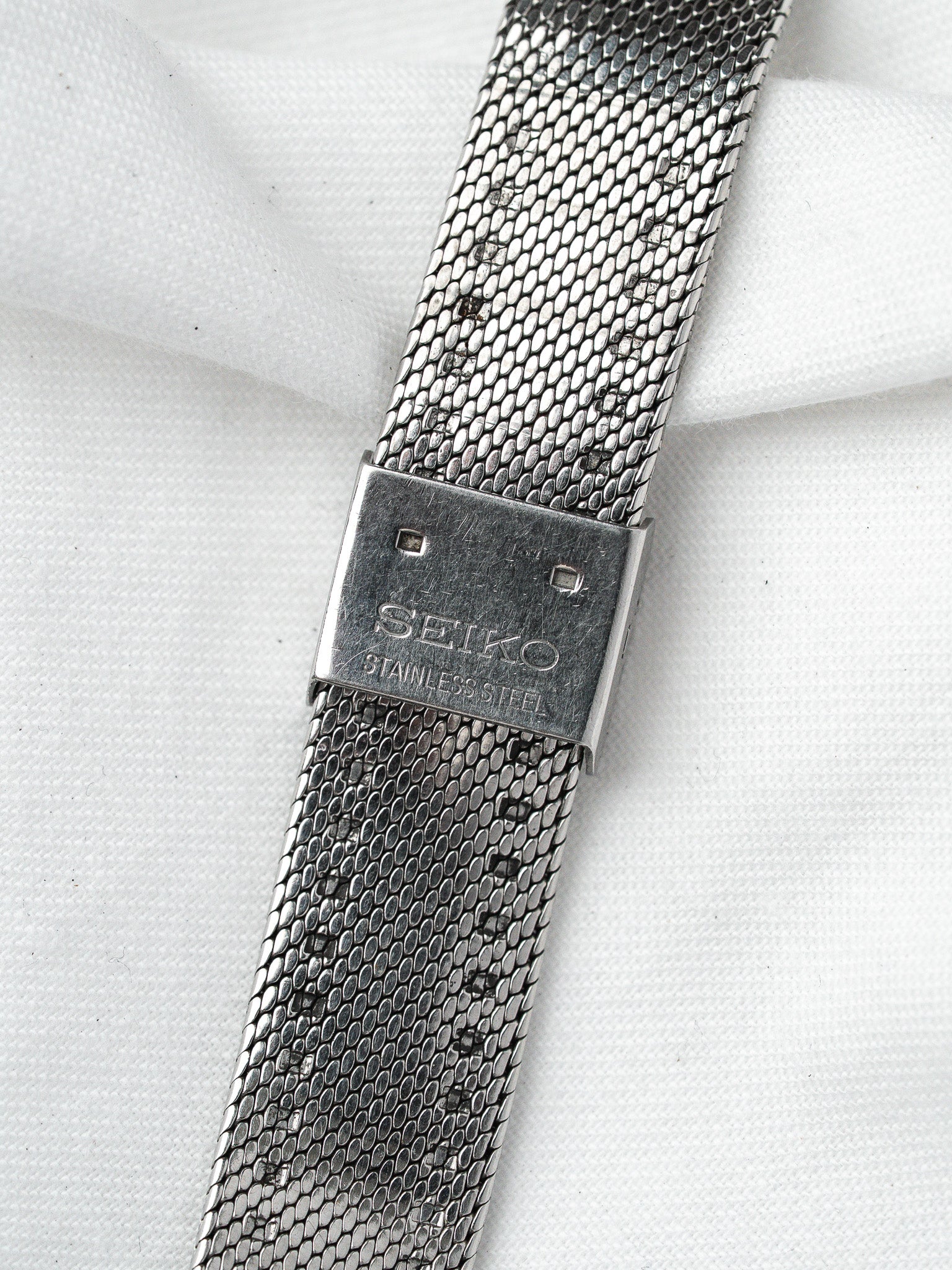 Seiko stainless steel mesh bracelet with engraved clasp on white fabric