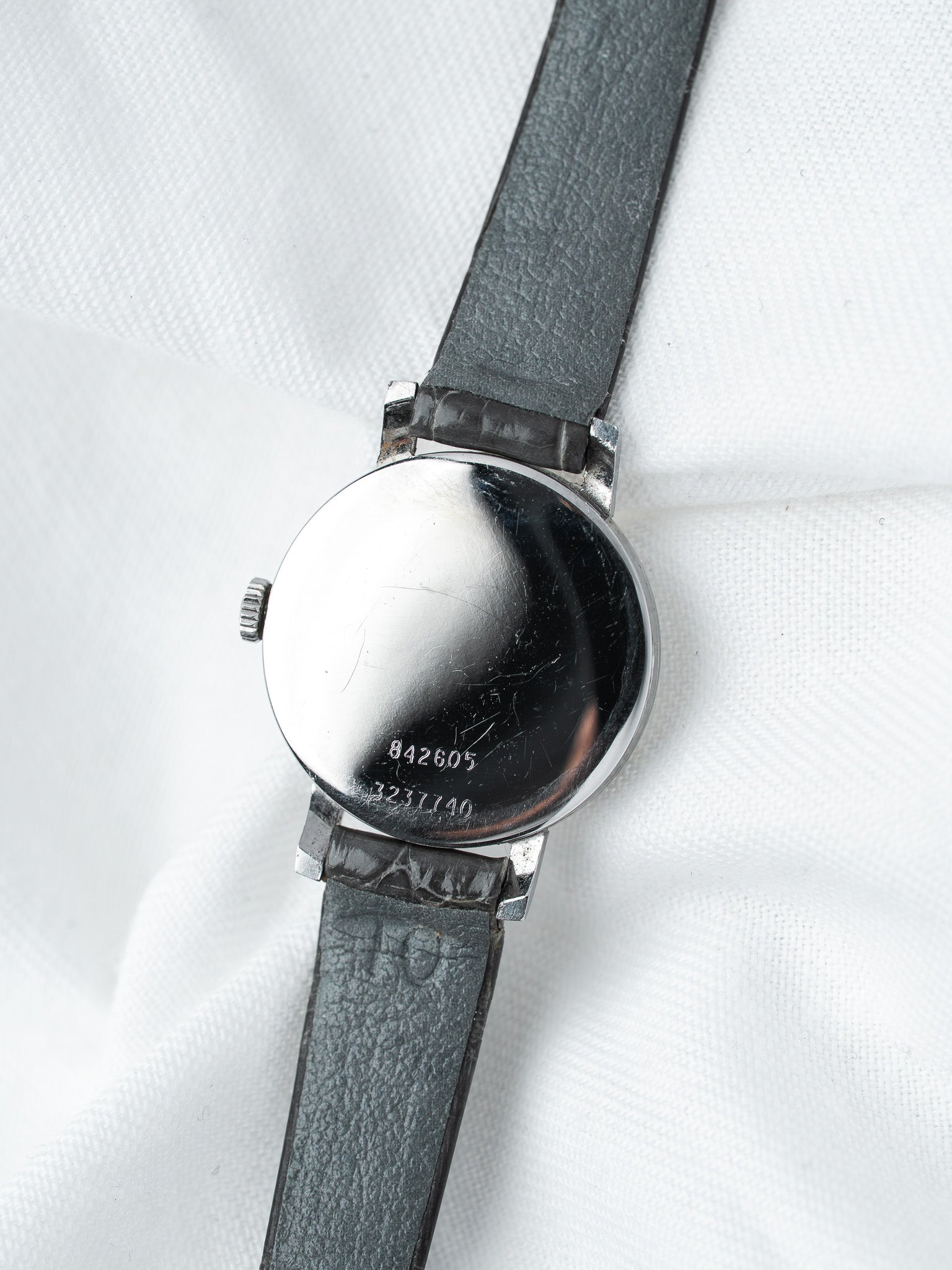 Vintage Omega watch back with serial numbers, steel case, black leather strap on white fabric