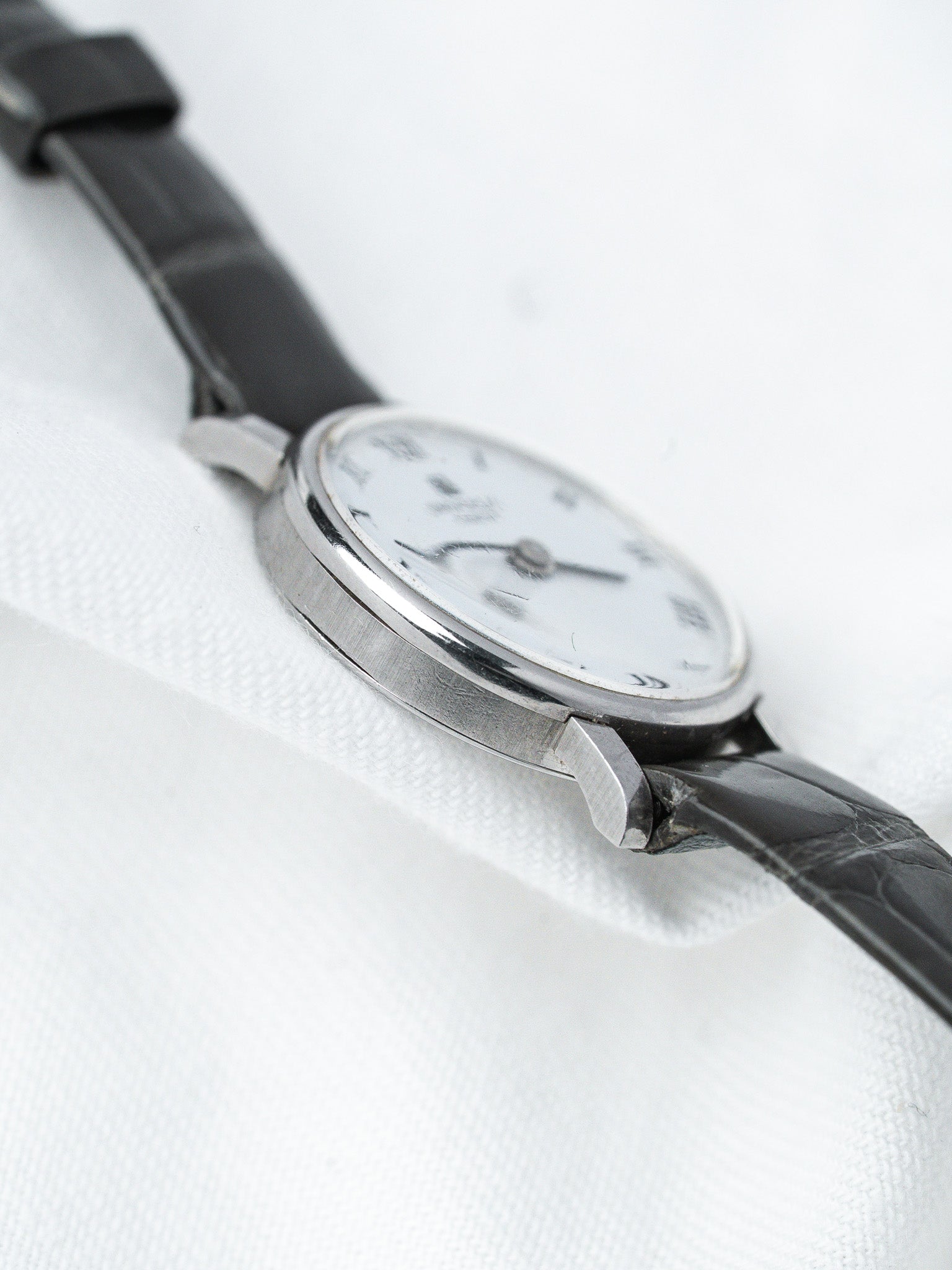Vintage Omega watch with white dial, steel case, black leather strap on white fabric