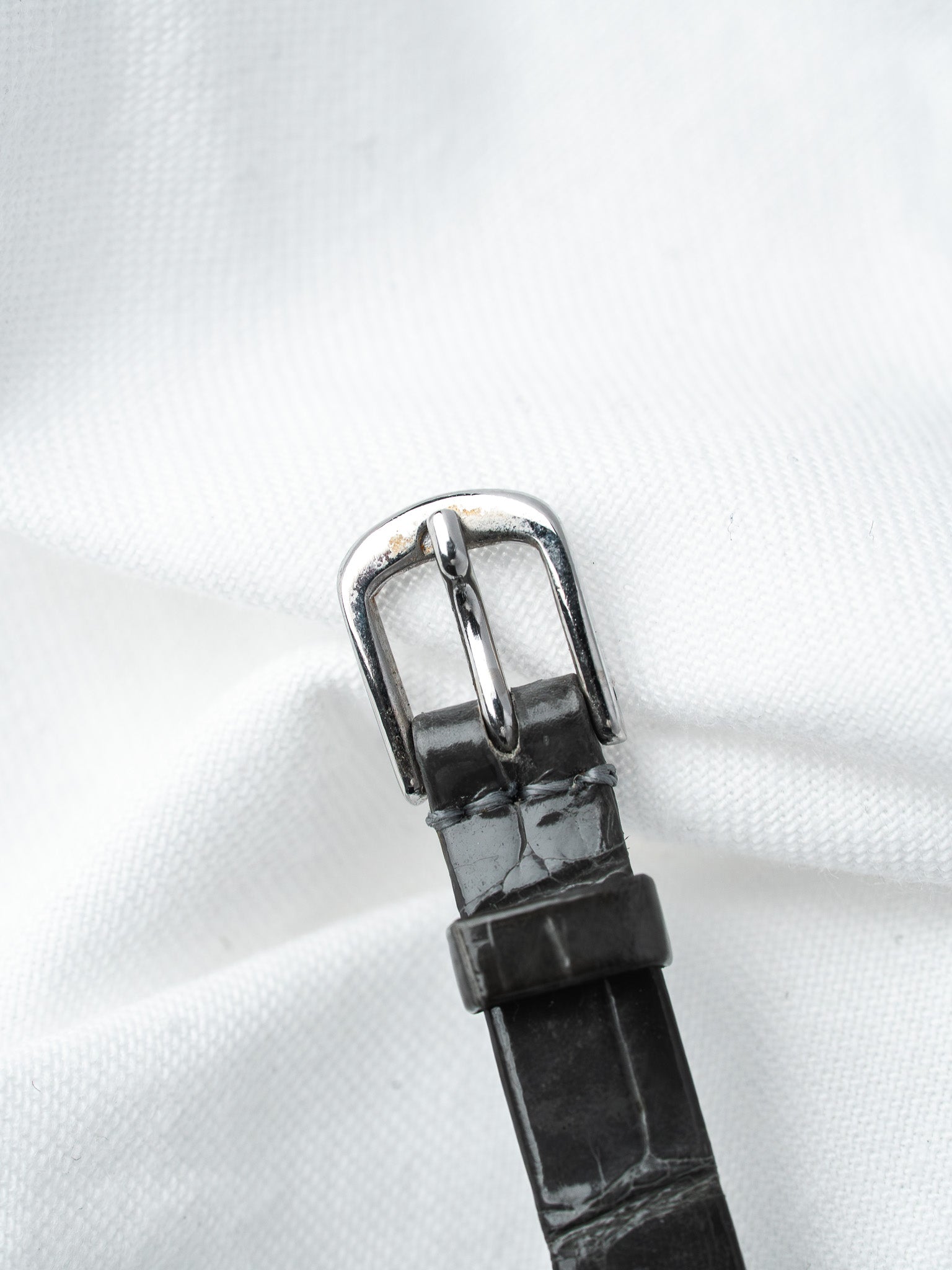 Black alligator leather watch strap with polished silver buckle on white fabric