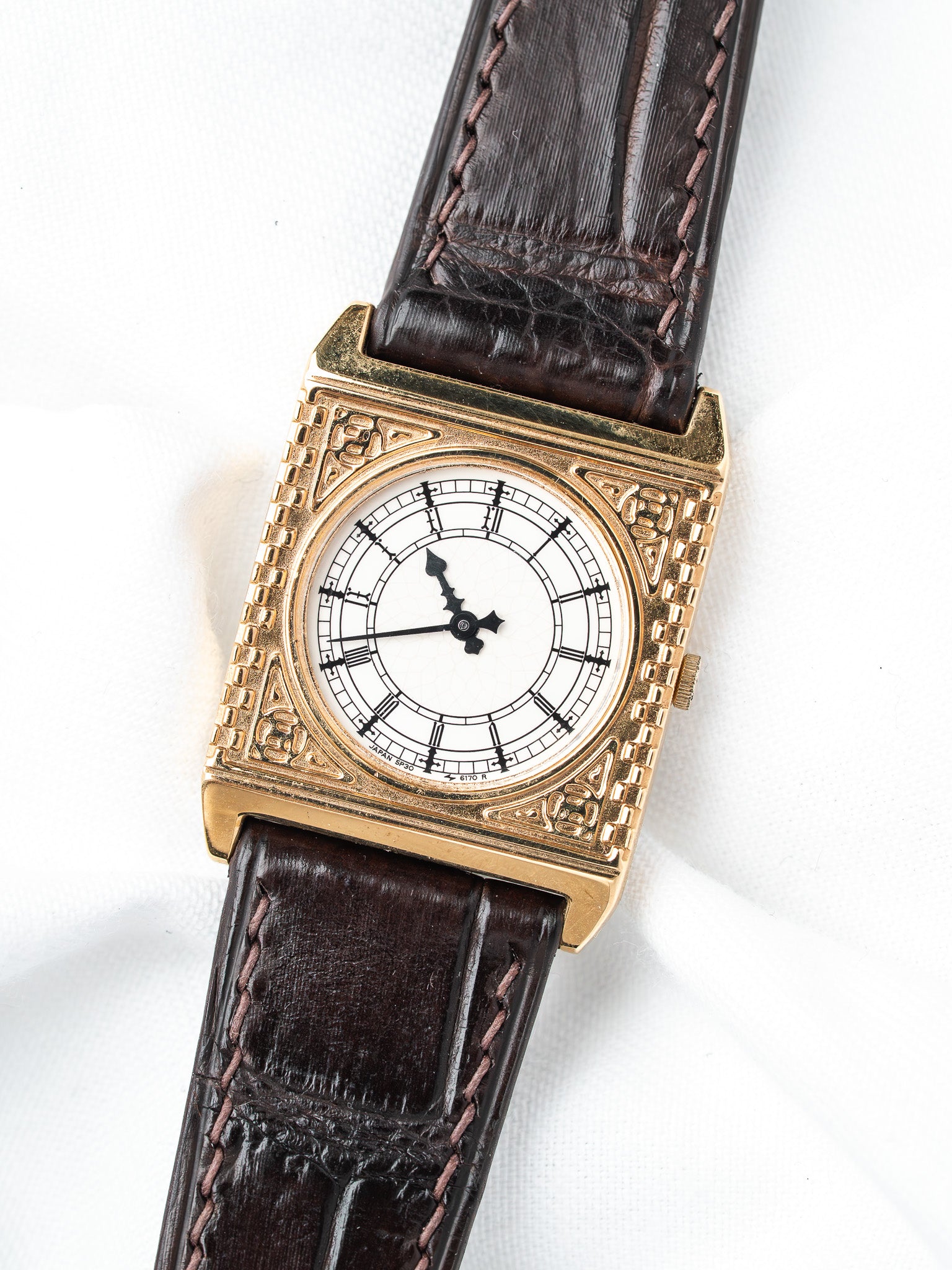 Vintage gold watch with white dial, brown leather strap, ornate square case