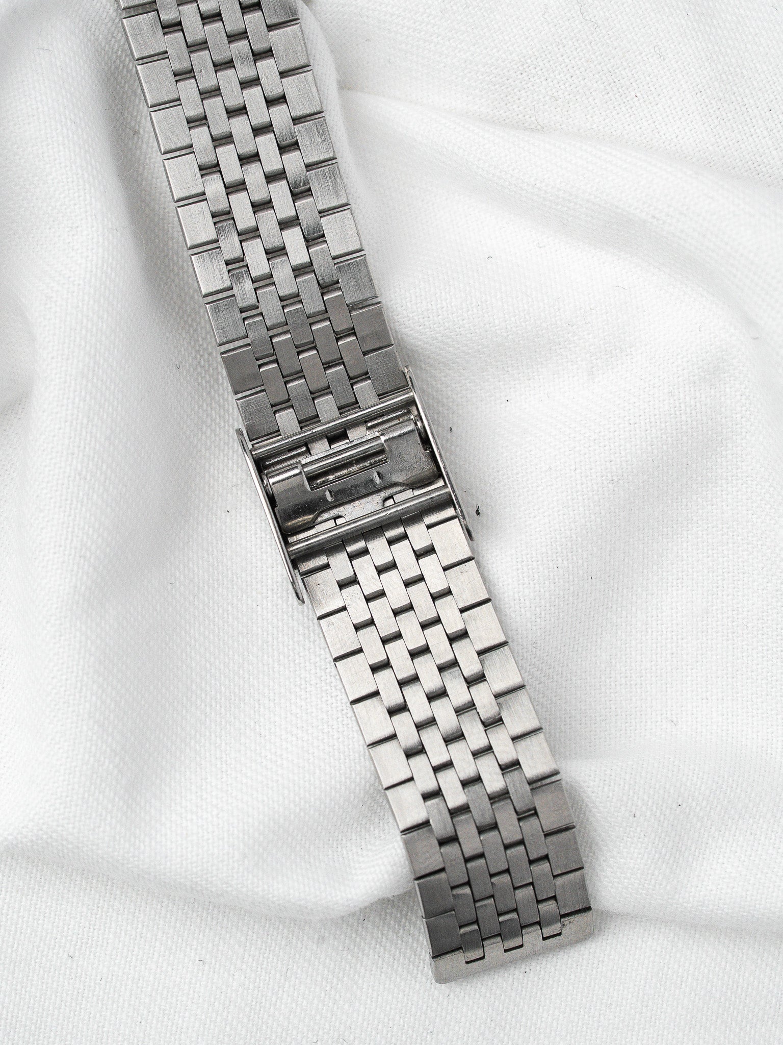 Vintage steel watch bracelet with intricate link design on white fabric