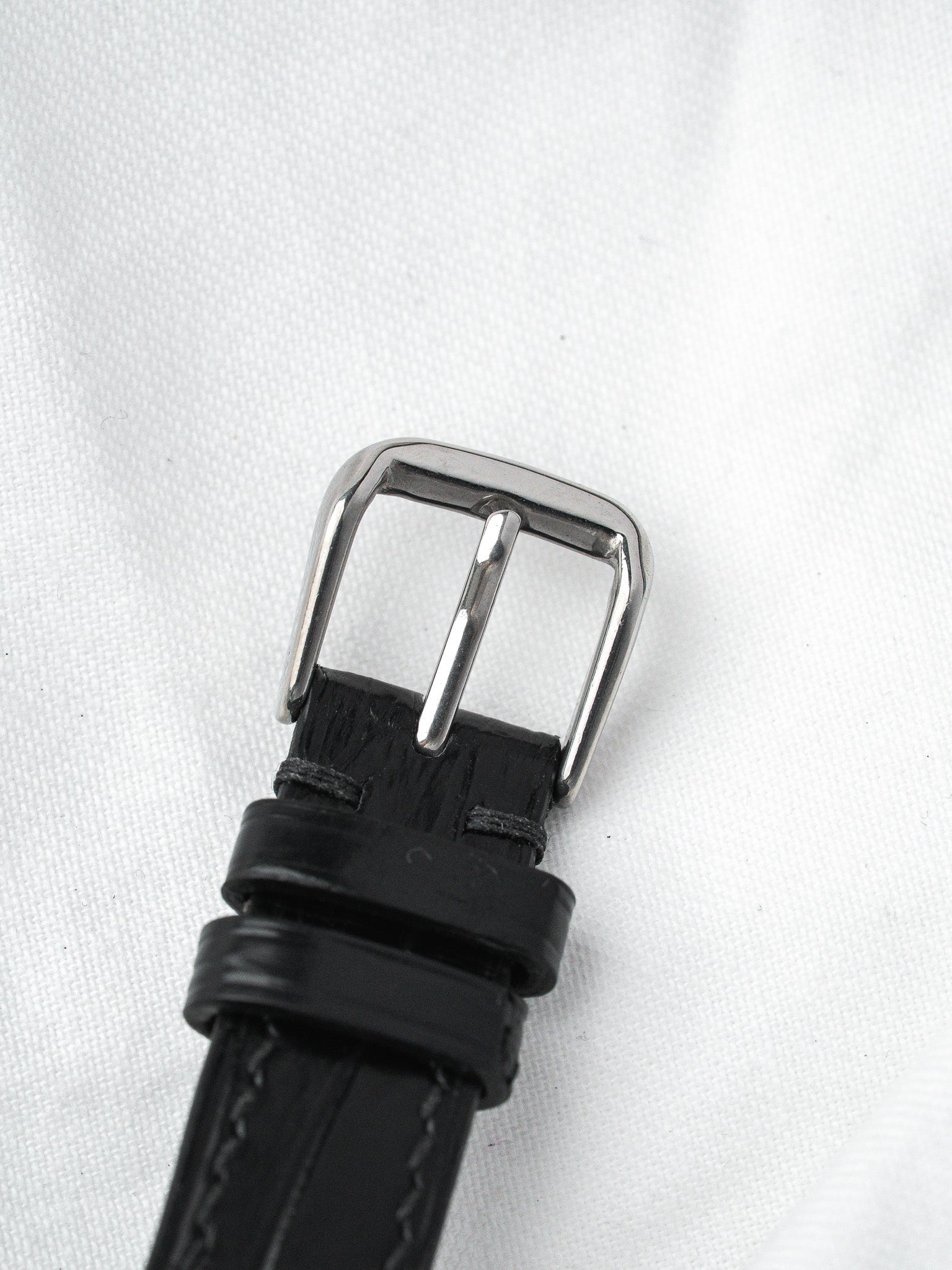 Black leather watch strap with polished silver buckle on white background