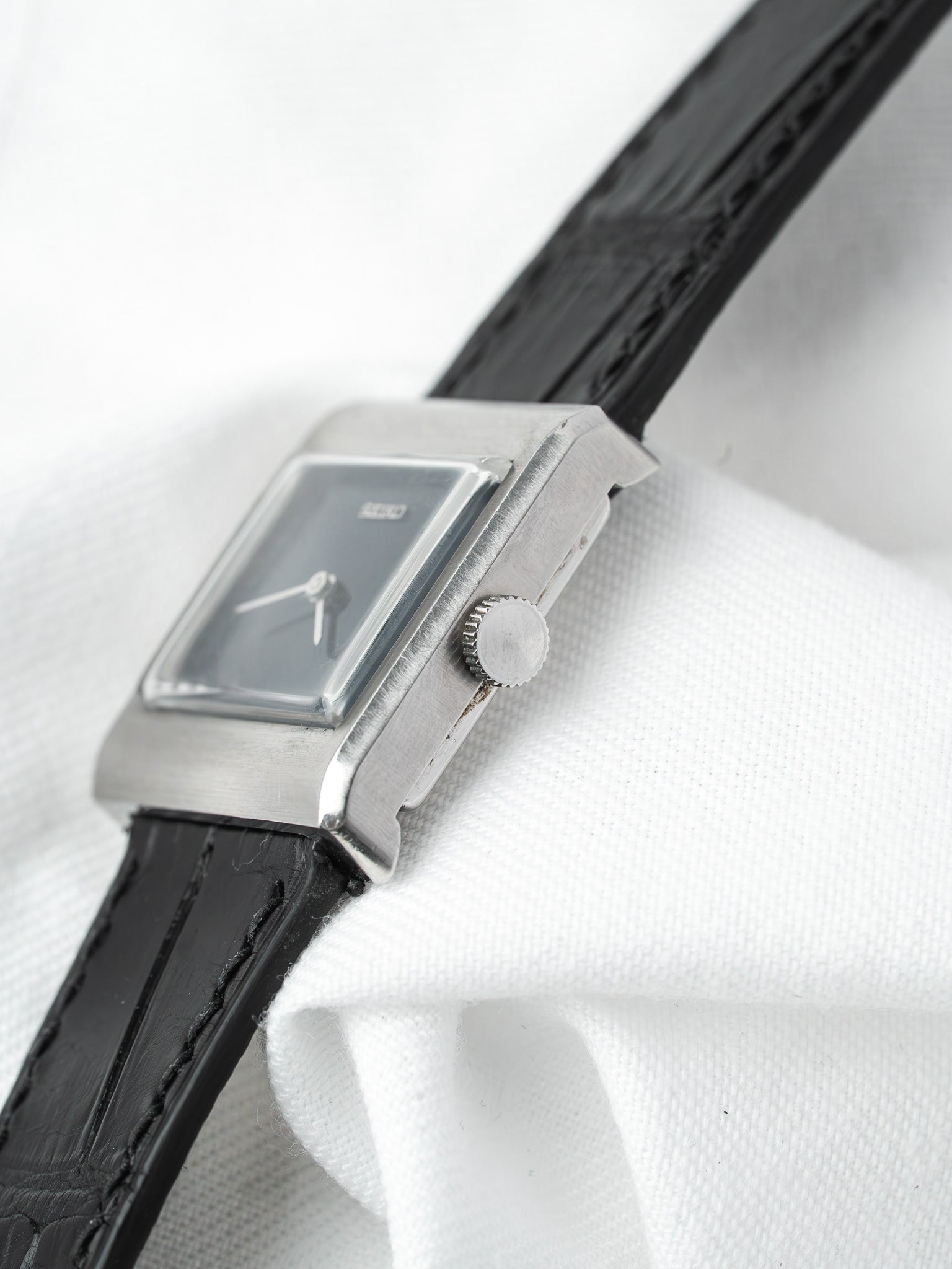 Vintage Seiko rectangular watch with silver case, black dial, and black leather strap on white fabric