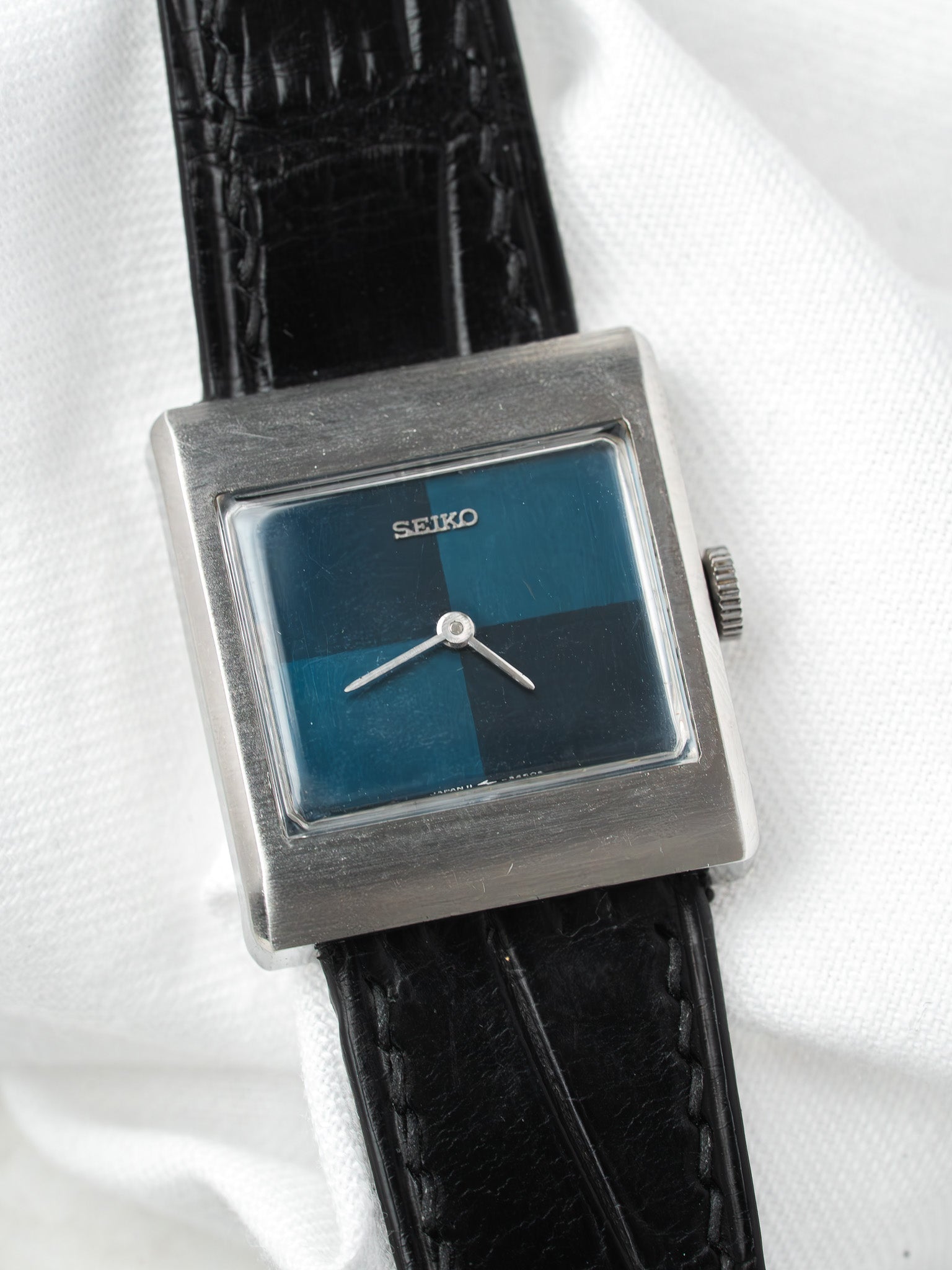 Seiko vintage square watch with blue-black dial, steel case, black leather strap on white fabric