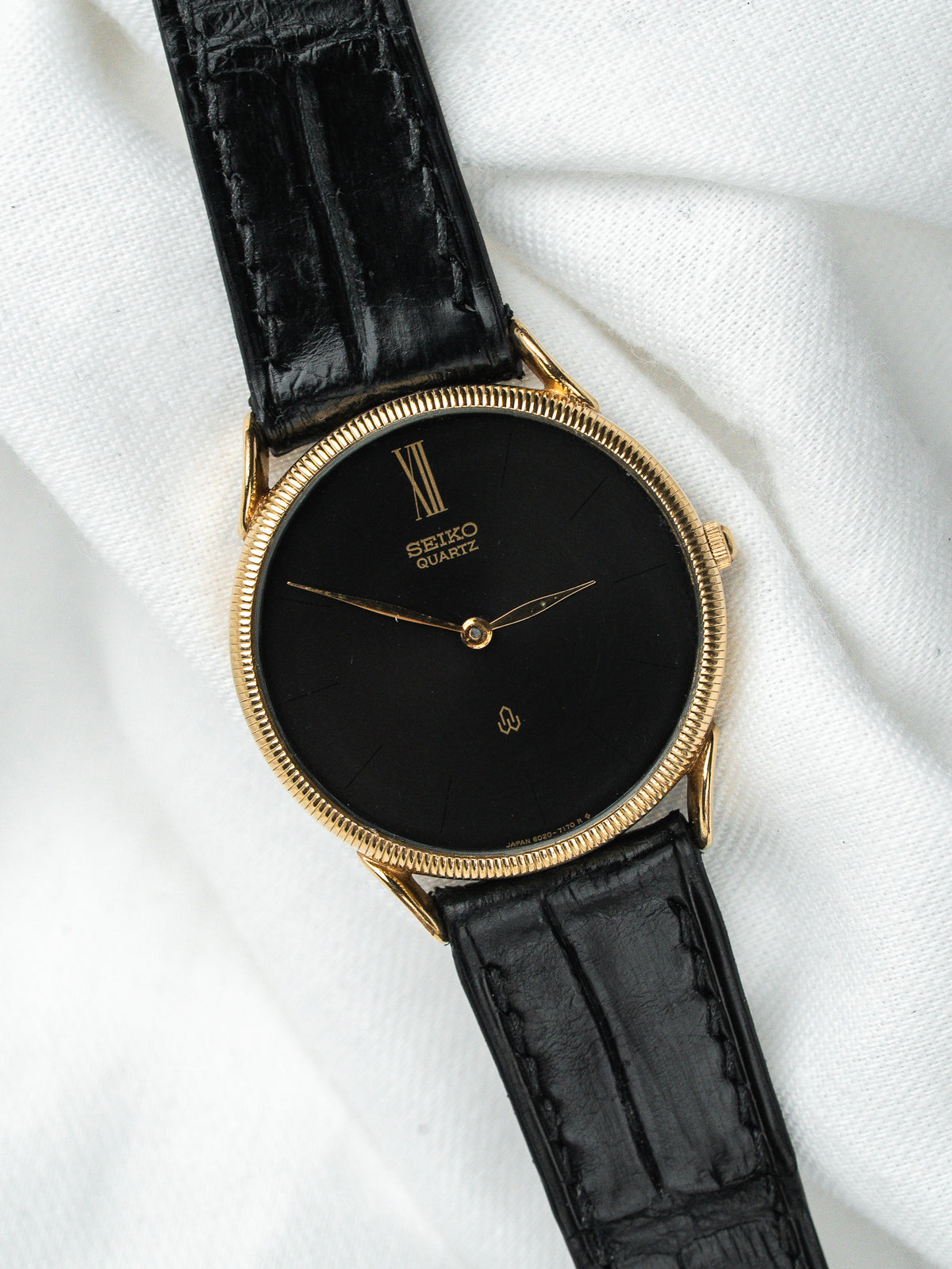 Montre Seiko Quartz vintage, boîtier doré, cadran noir et bracelet en cuir noir
