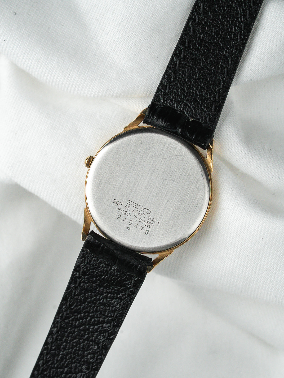 Dos d'une montre Seiko vintage en acier et or avec bracelet cuir noir