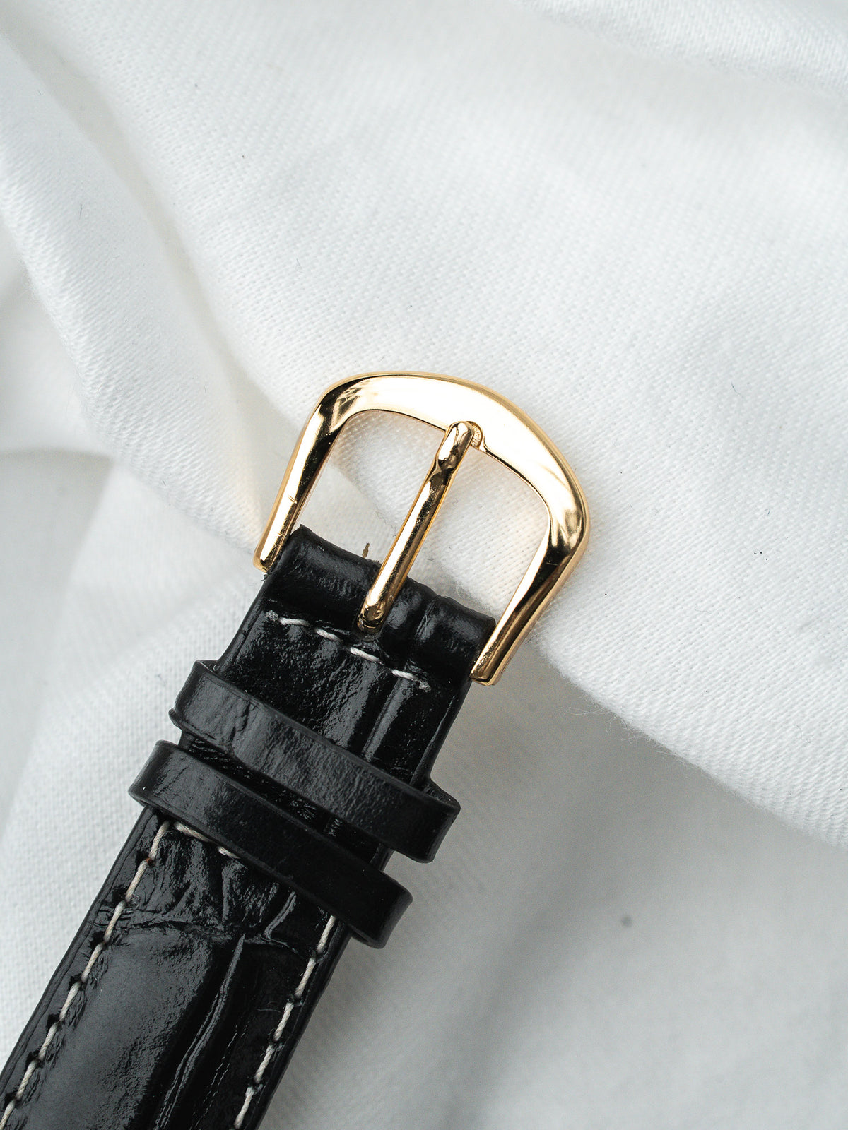 Boucle dorée d'un bracelet de montre en cuir noir grainé sur fond blanc