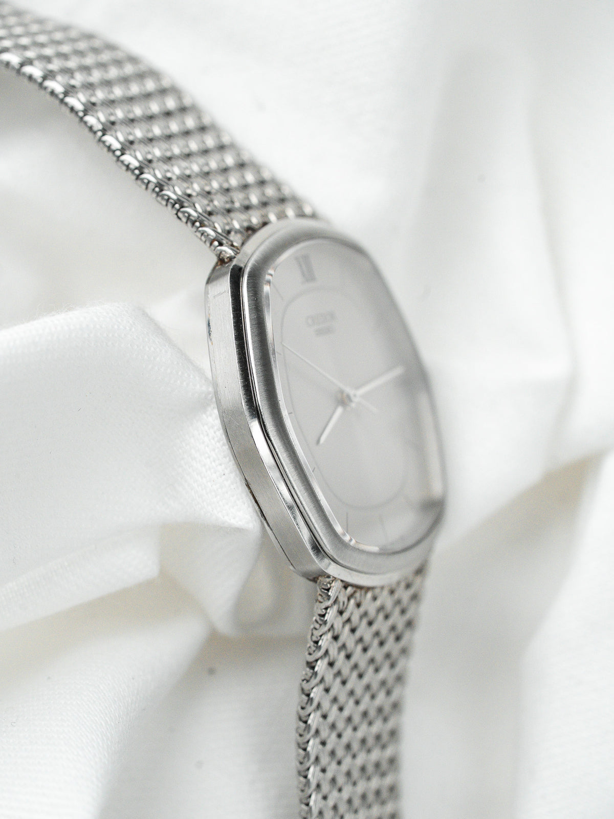 Montre vintage en acier au boîtier ovale et bracelet maille milanaise sur fond blanc